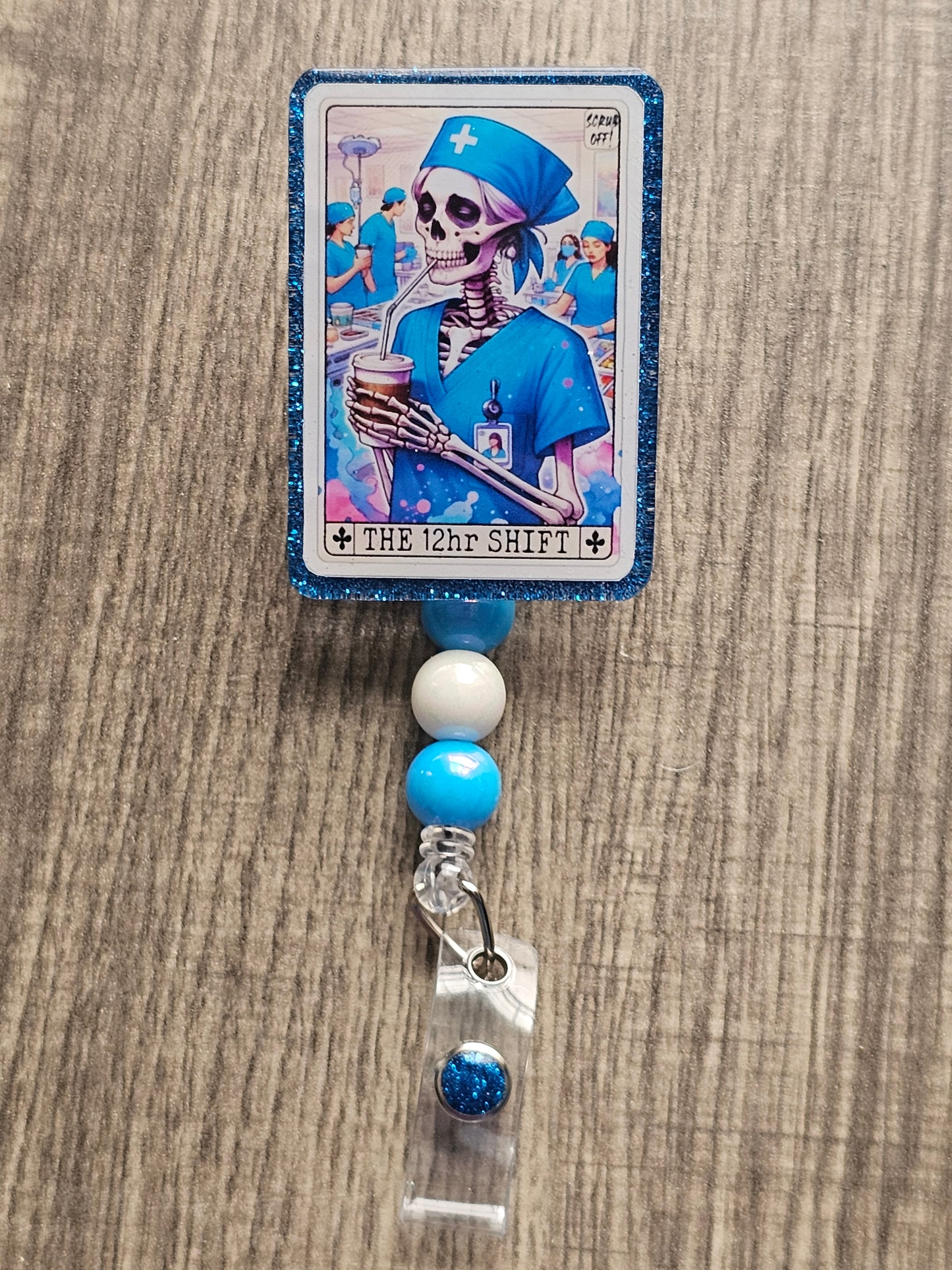 A badge Reel in the shape and design of a tarot card featuring a skeleton nurse drinking some coffee in a hospital. The Badge holder being titled "The 12Hr Shift.