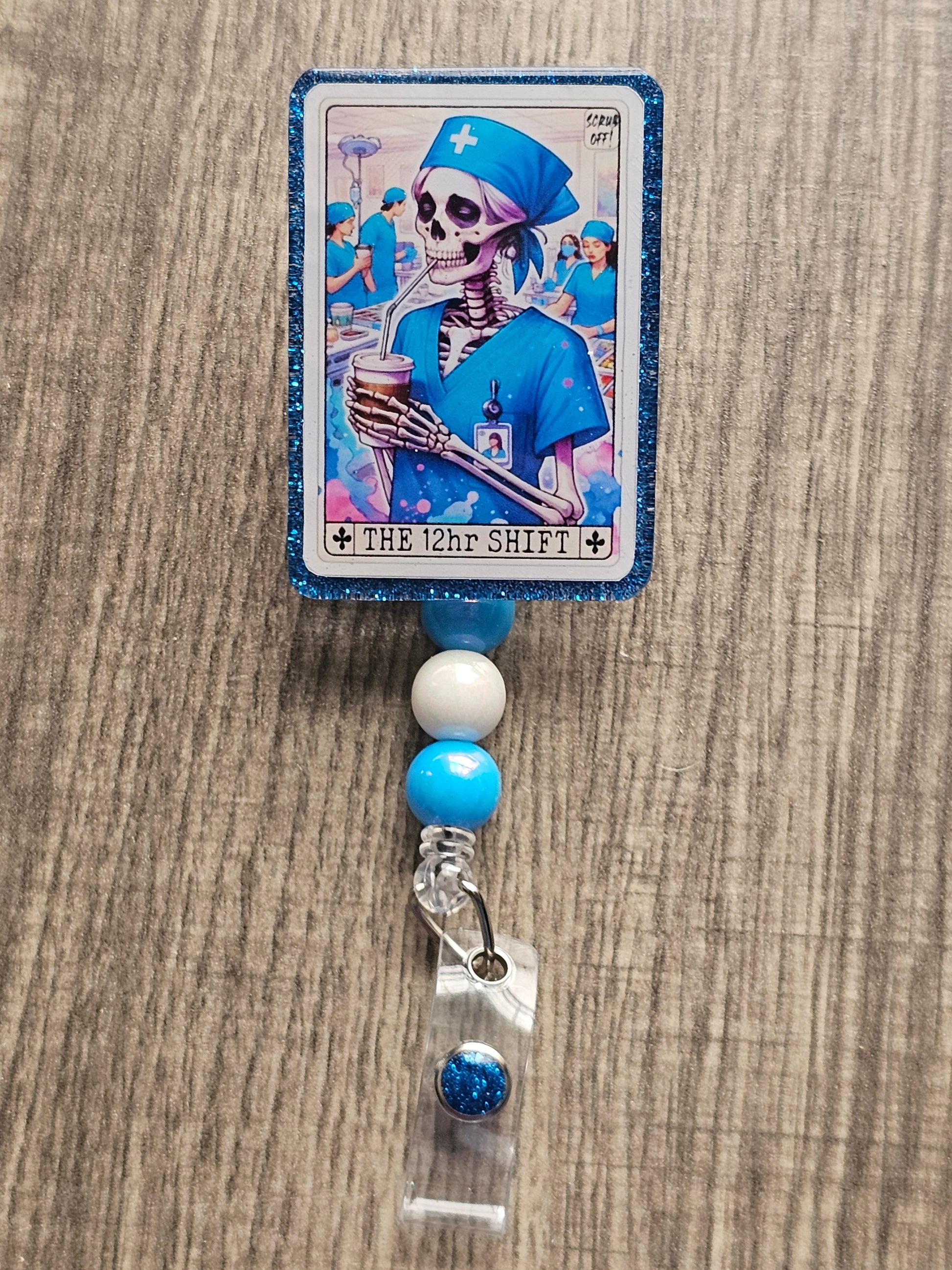 A badge Reel in the shape and design of a tarot card featuring a skeleton nurse drinking some coffee in a hospital. The Badge holder being titled "The 12Hr Shift.