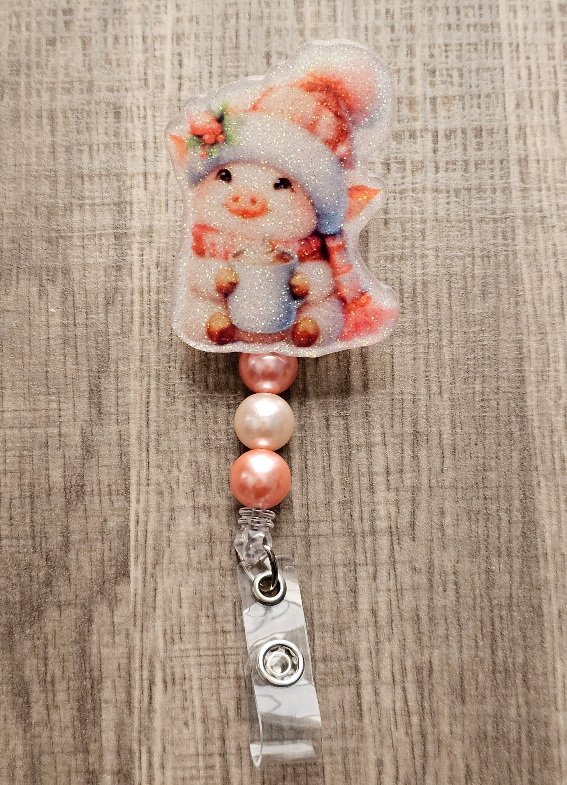 A badge reel featuring an adorable piglet dressed in a cheerful holiday hat and scarf, this delightful design showcases the piglet holding a steaming cup of cocoa with an irresistible smile.