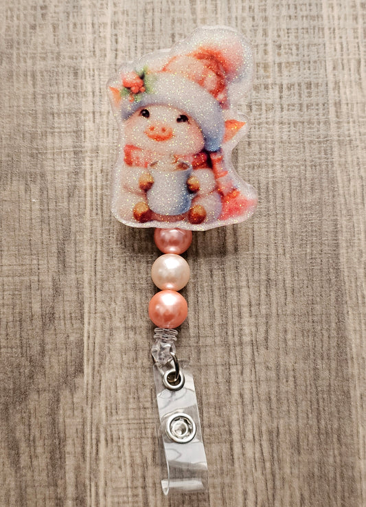 A badge reel featuring an adorable piglet dressed in a cheerful holiday hat and scarf, this delightful design showcases the piglet holding a steaming cup of cocoa with an irresistible smile.