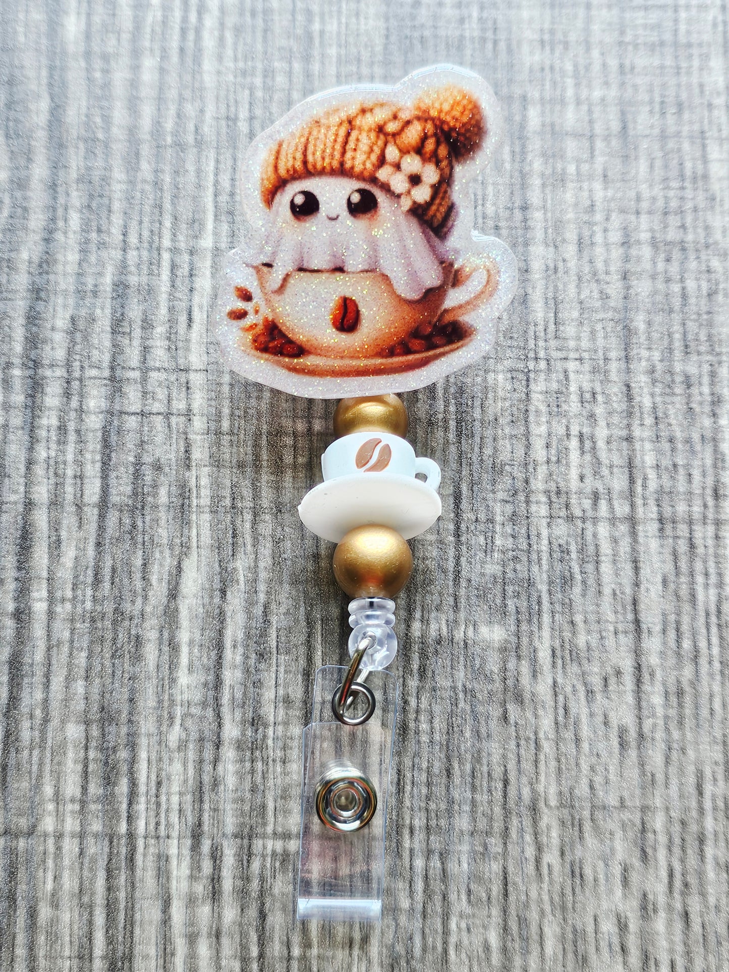 Adorable ghost in a coffee cup with a fall hat on a retractable badge reel with coffee and gold beads.