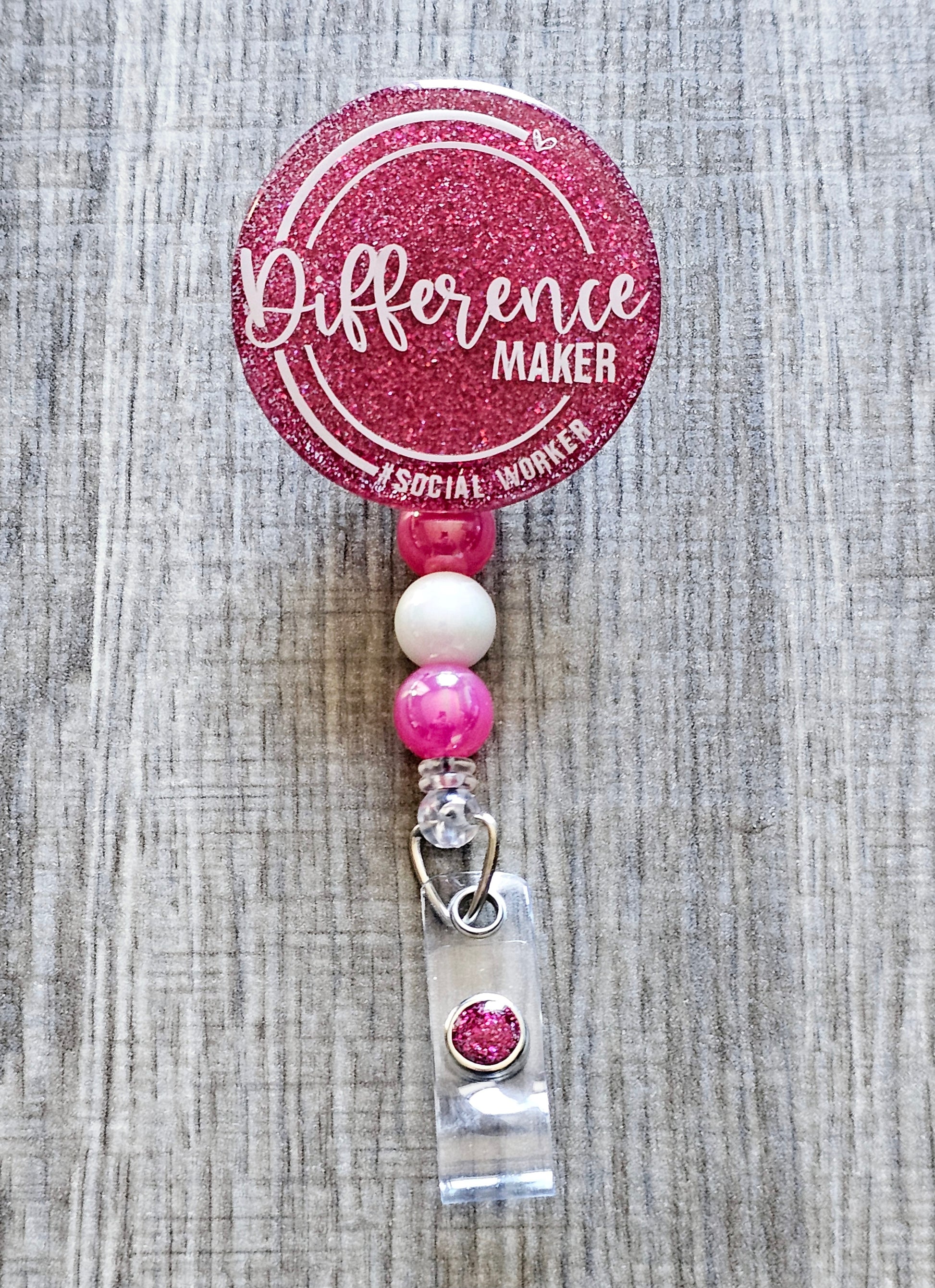 Social work-themed badge reel with "Difference Maker – #SocialWorker" printed on a glittery background, available in multiple colors.