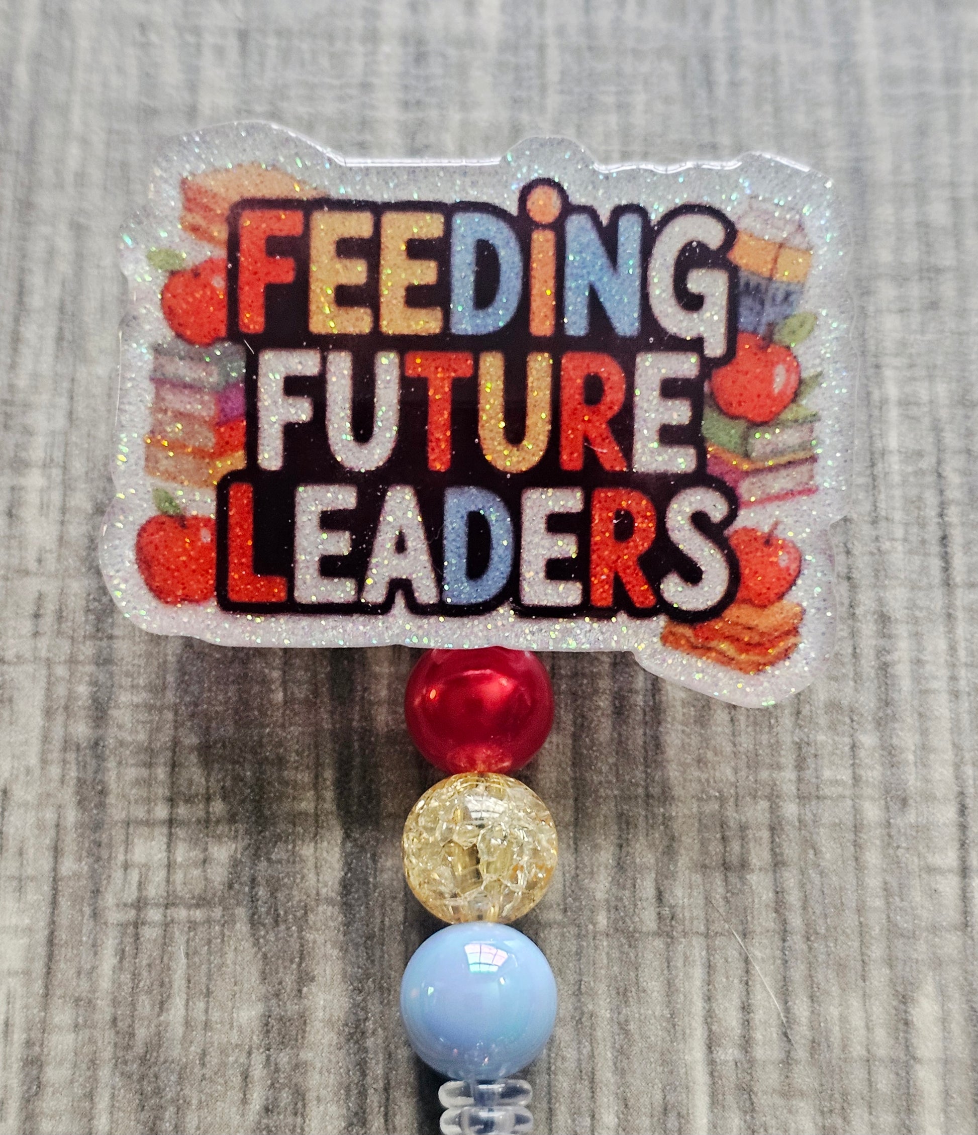 Badge reel with the words "Feeding Future Leaders" in a creative, colorful manner, surrounded by books and apples, with creatively matching decorative beads.