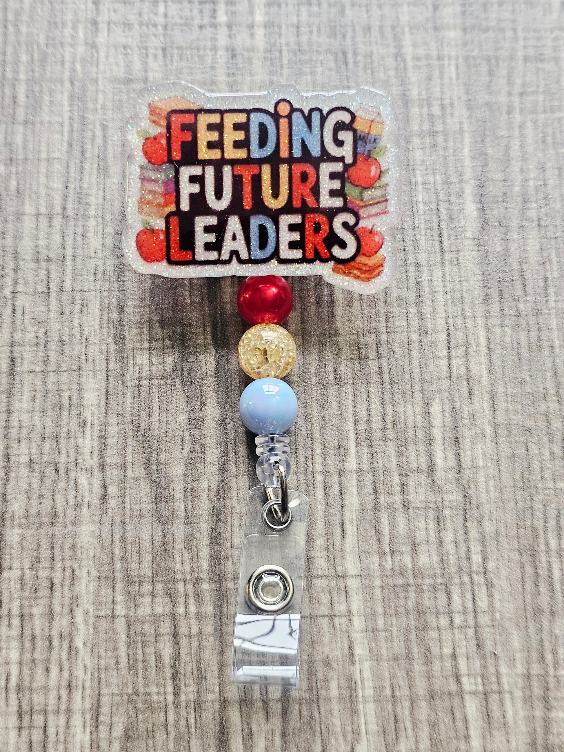 Badge reel with the words "Feeding Future Leaders" in a creative, colorful manner, surrounded by books and apples, with creatively matching decorative beads.