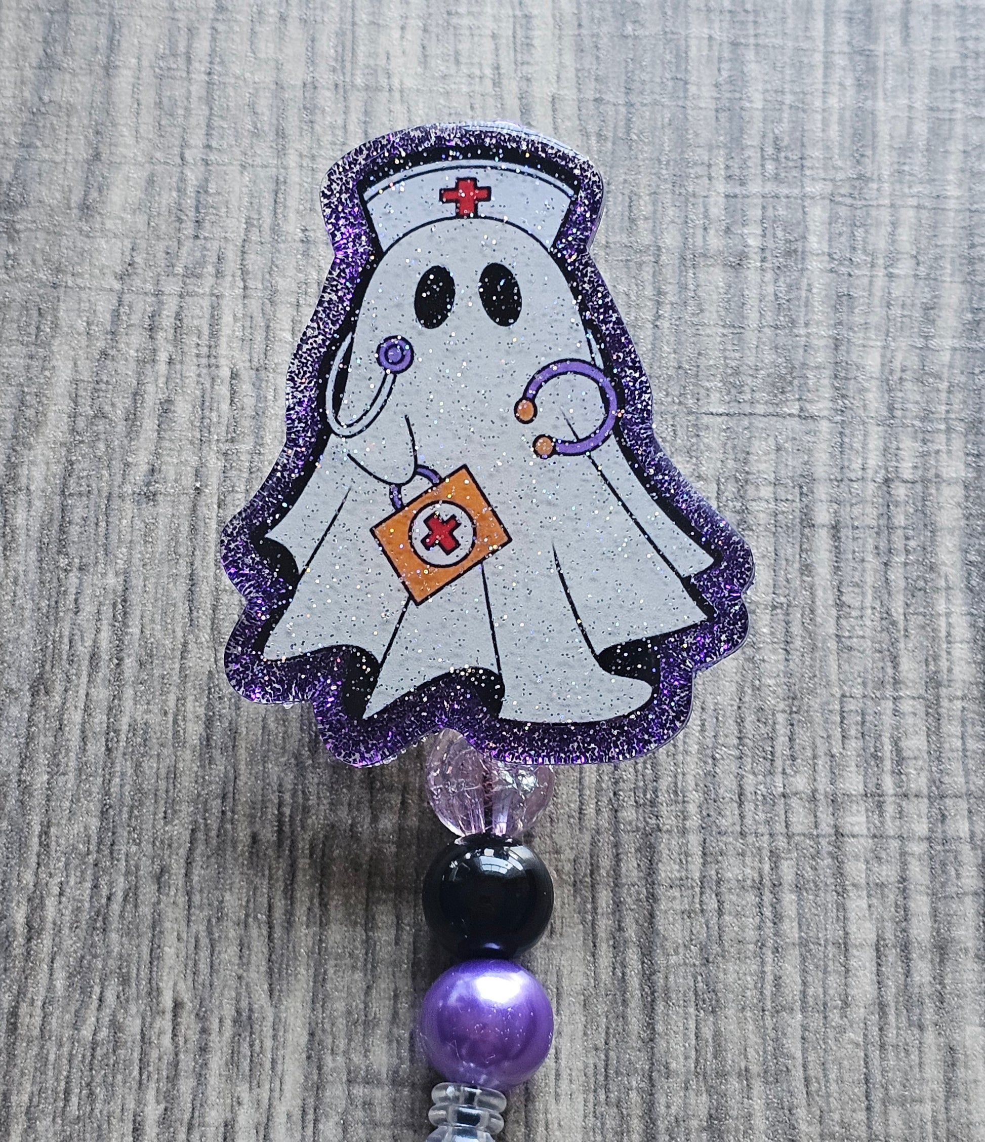 a badge reel shaped as a ghost with the design of a ghost nurse with a nursing hat, stethoscope along with a first aid kit