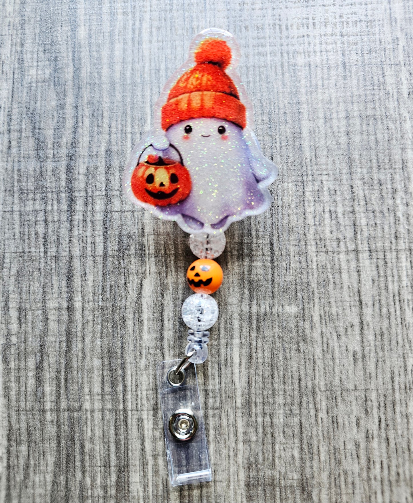 Cute ghost with an orange fall hat and a jack-o'-lantern trick-or-treat bucket on a Halloween-themed badge reel.
