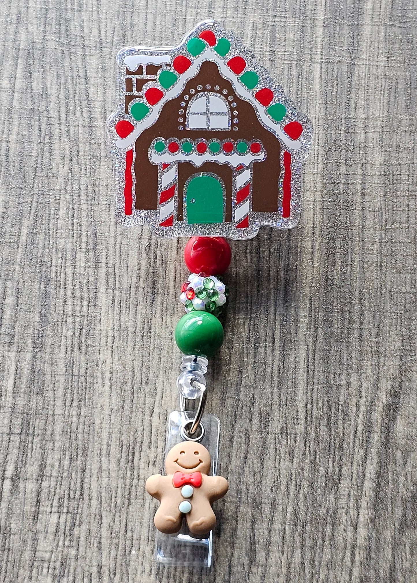 A badge reel that is shaped as a gingerbread house accompanied by a gingerbread man on the clip portion of the badge reel