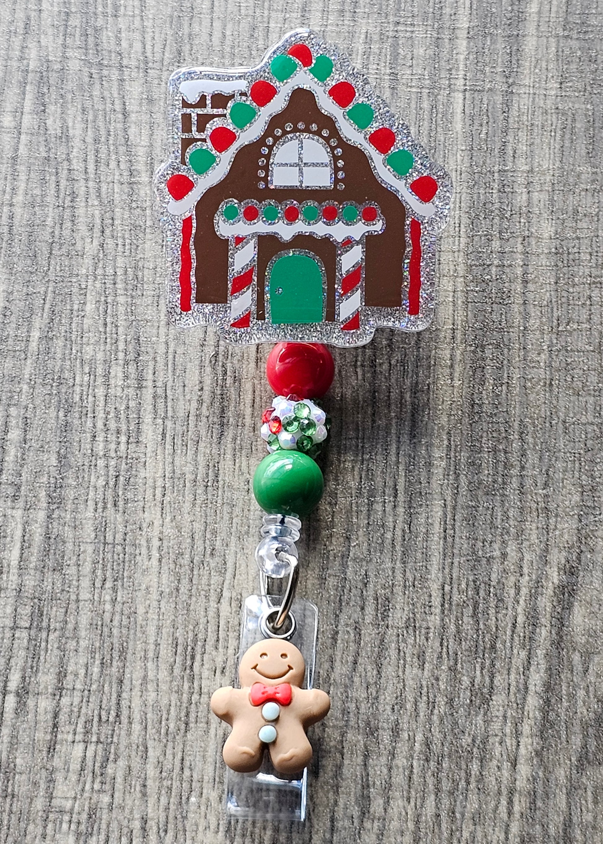 A badge reel that is shaped as a gingerbread house accompanied by a gingerbread man on the clip portion of the badge reel