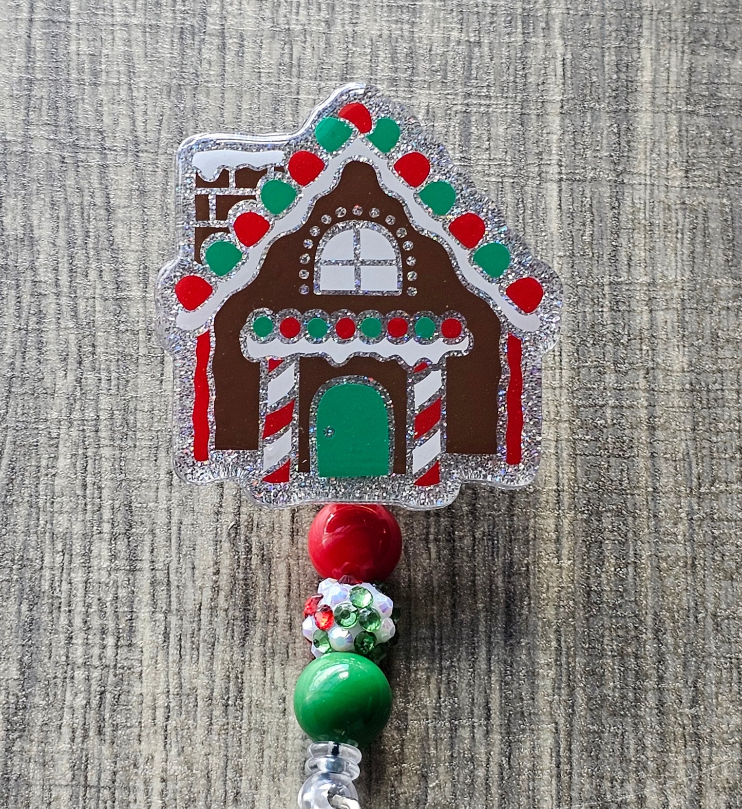 A badge reel that is shaped as a gingerbread house accompanied by a gingerbread man on the clip portion of the badge reel