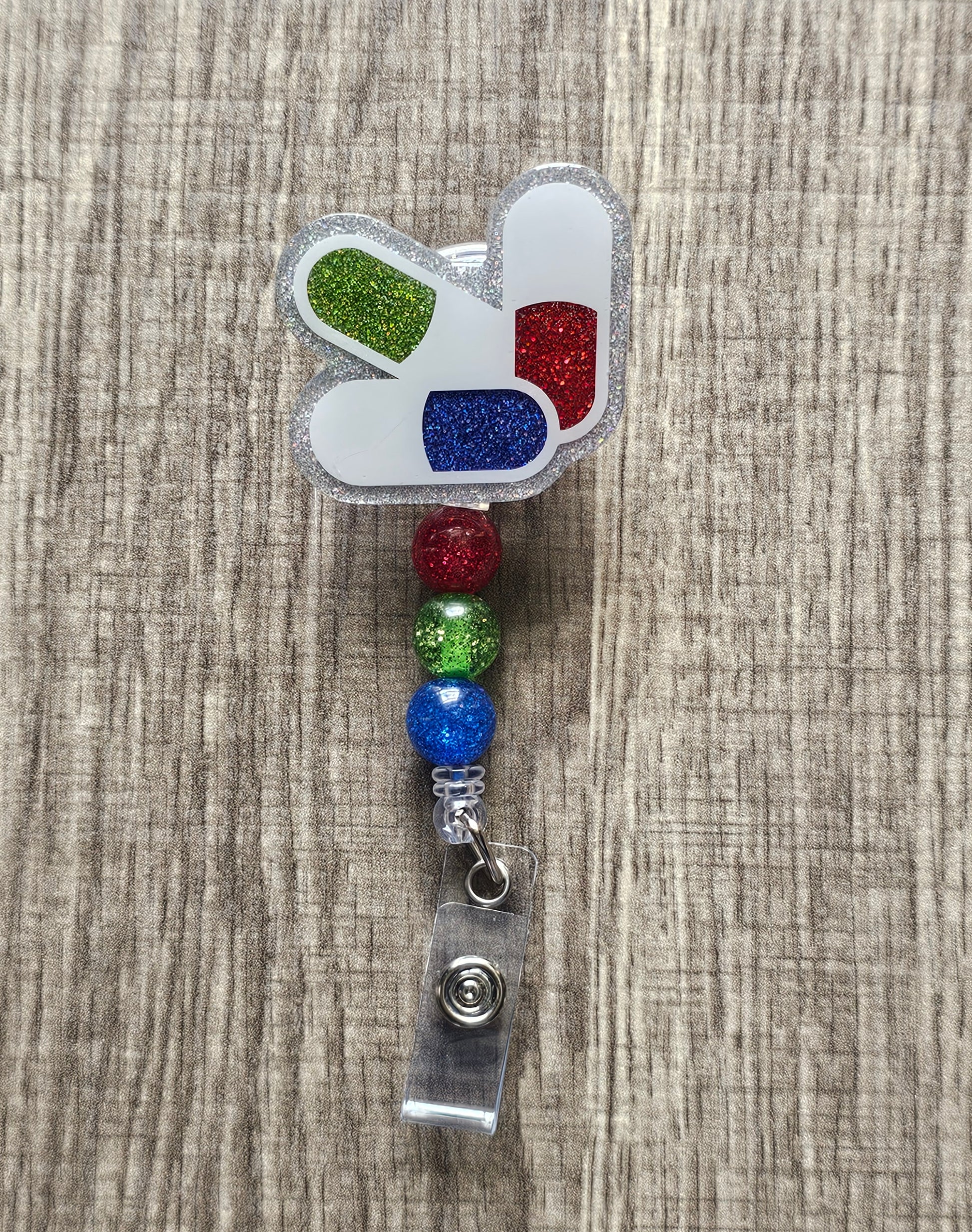 Badge reel shaped like 3 glitter pills: green, red, and blue.