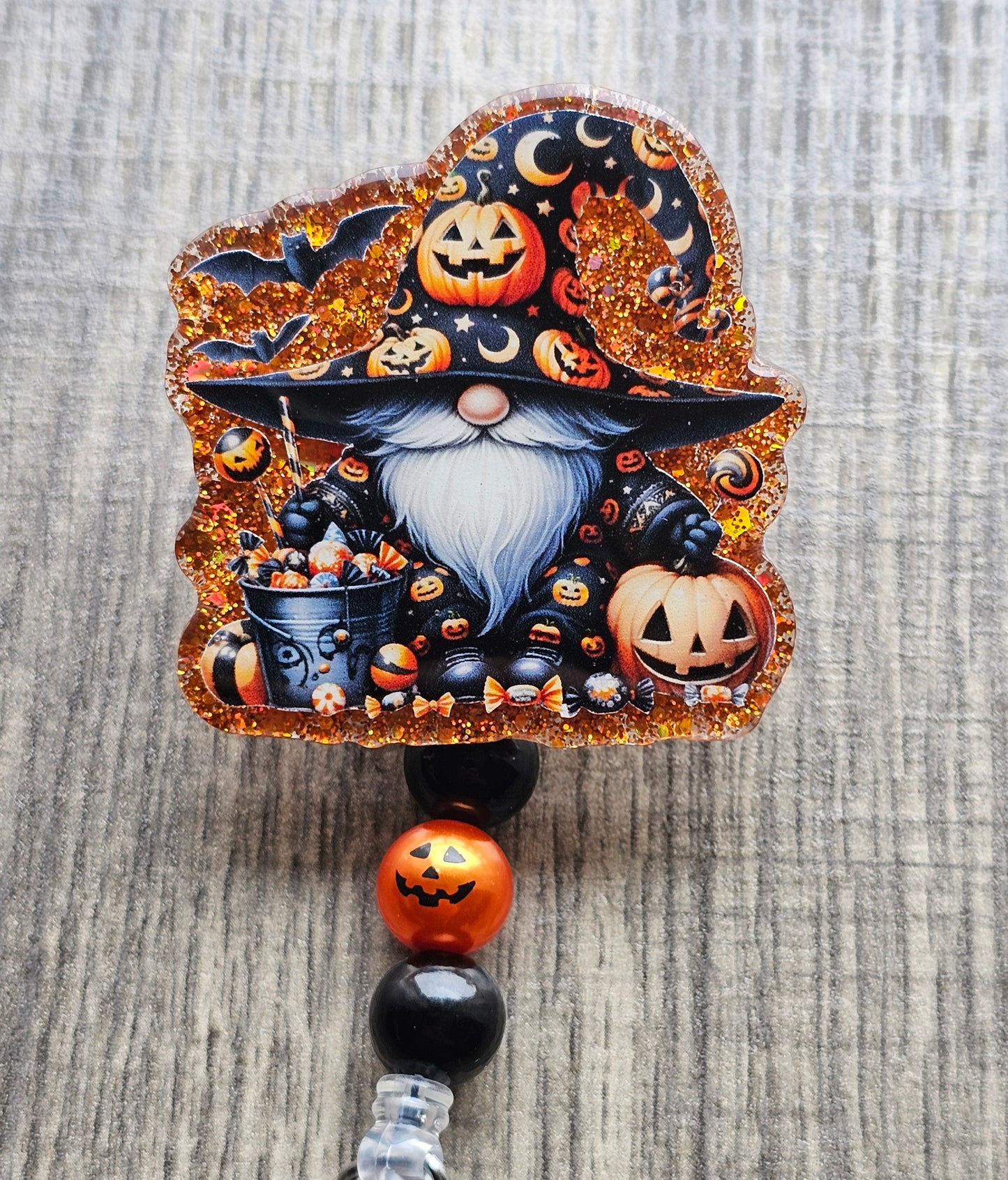 Gnome in a wizard costume adorned with pumpkins beside a trick or treat bucket along with a jack-o-lantern