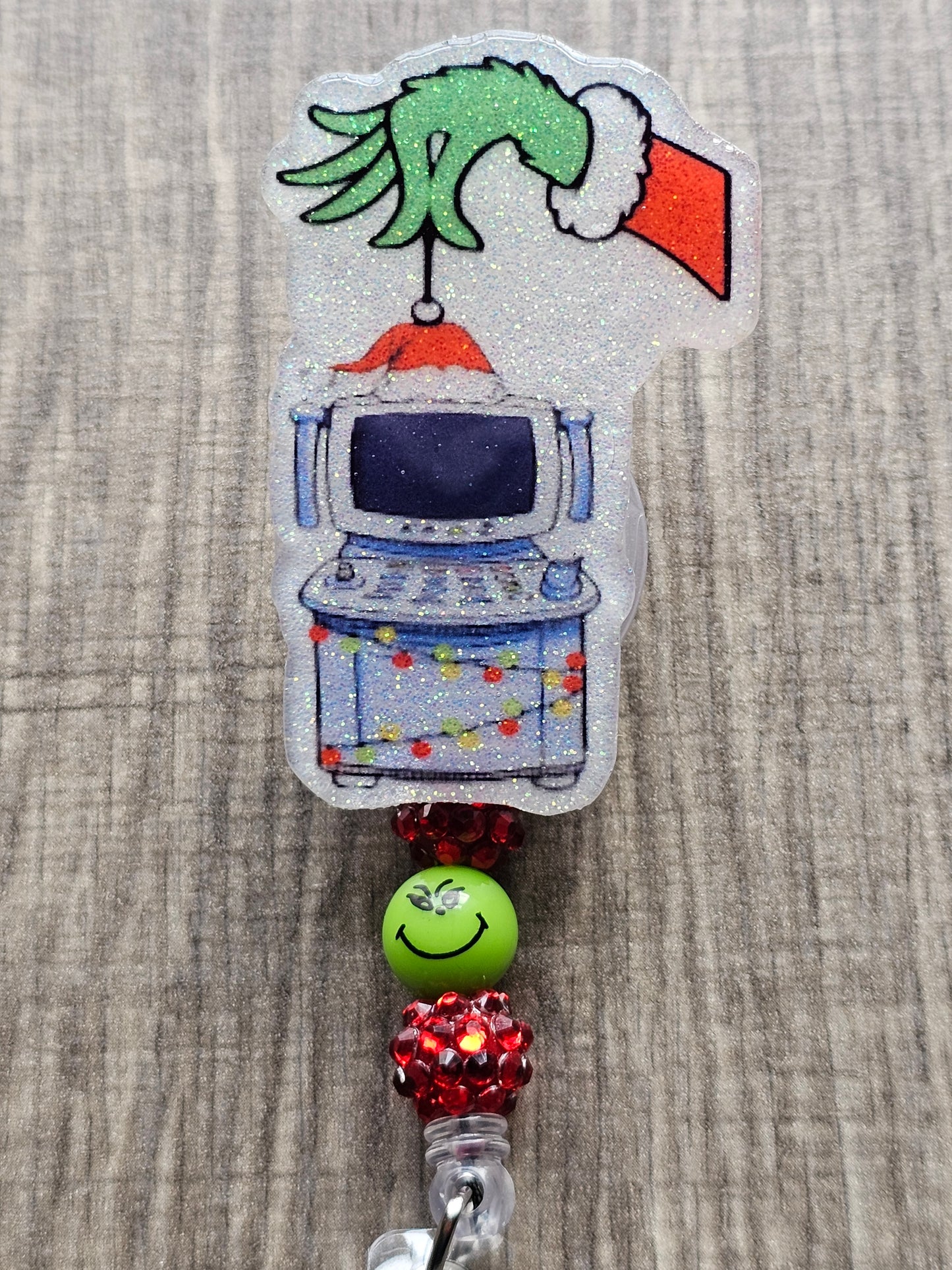 A badge reel displaying the hand of the grinch with a Christmas sweater holding an ultrasound machine adorned in Christmas Lights.