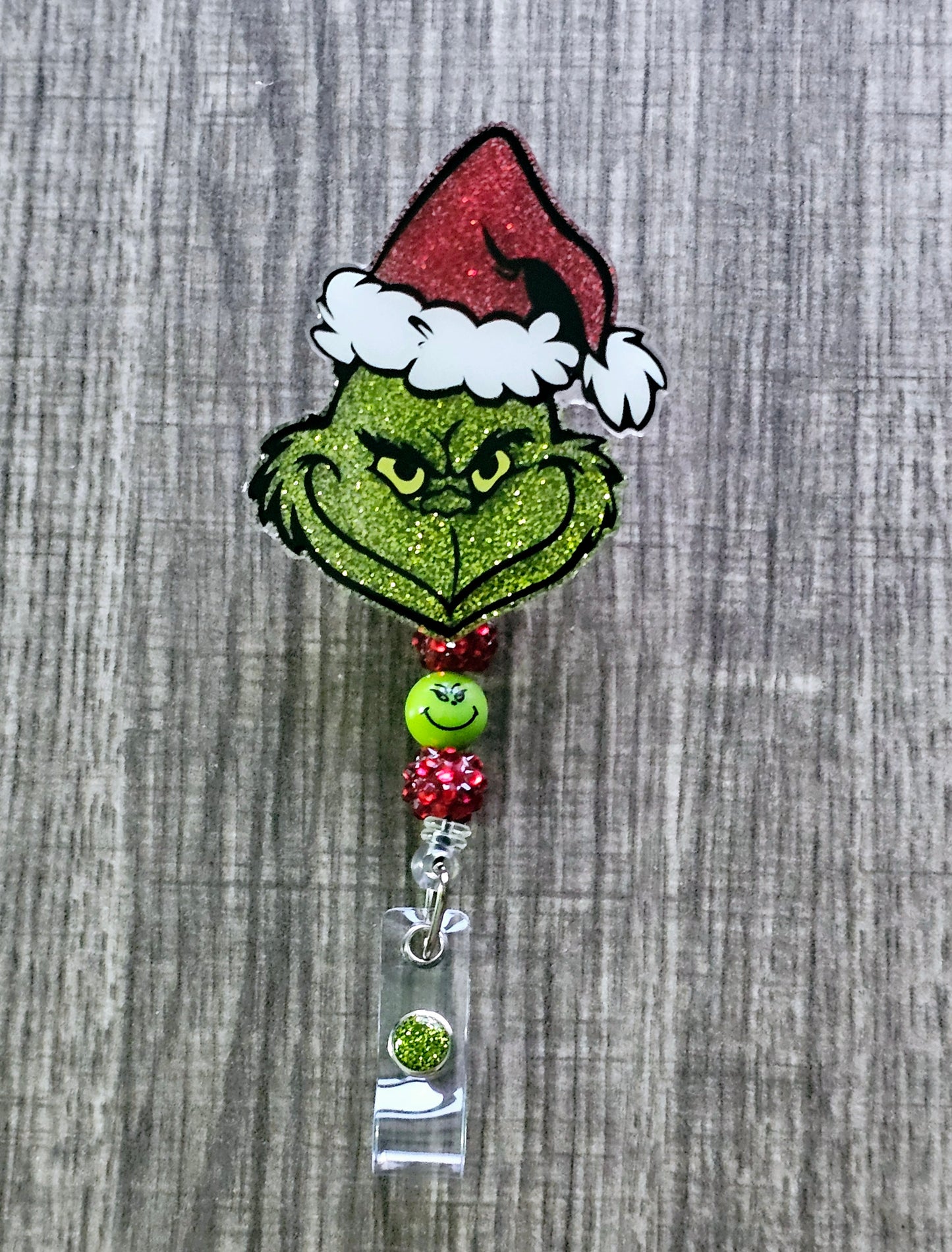A badge reel featuring the face of the grinch grinning while wearing a Christmas hat