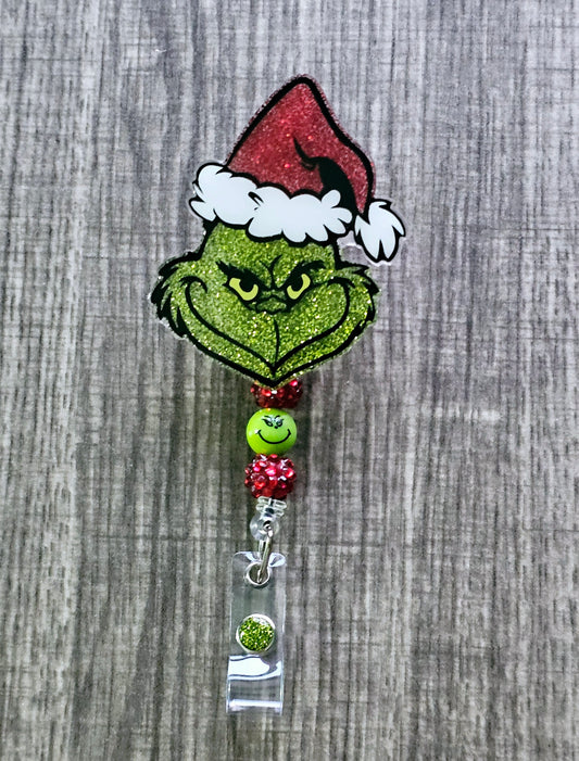A badge reel featuring the face of the grinch grinning while wearing a Christmas hat