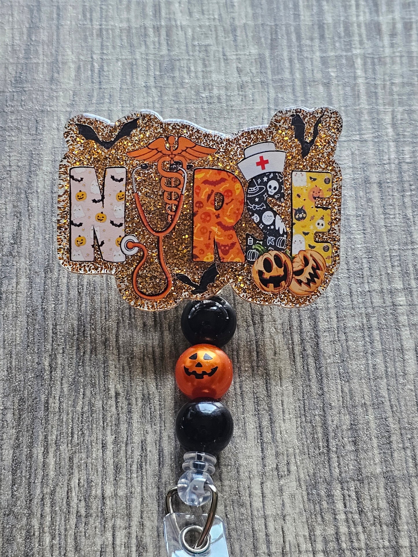 A badge reel with the word Nurse styled in a Halloween theme featuring bats evil jack-o-lanterns stethoscope and health symbol, along with a stethoscope in line with Halloween theme colors such as orange and black.