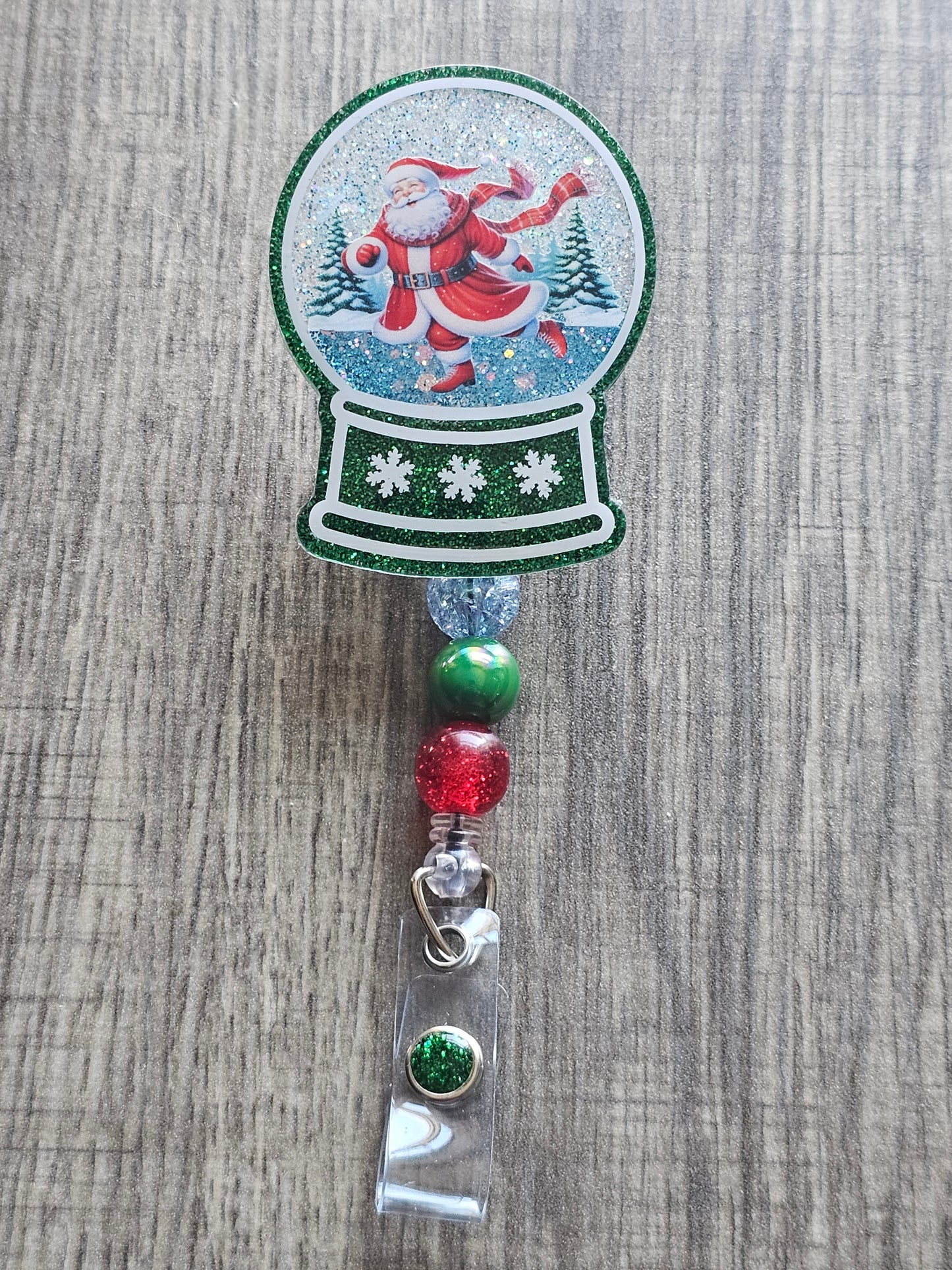 A badge reel with a snow globe design featuring Santa skating on Ice.