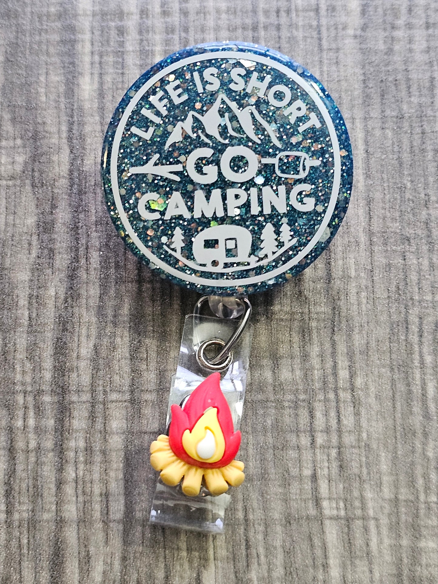 A Badge Reel featuring the statement life is short go camping with a peacock green background and camping décor