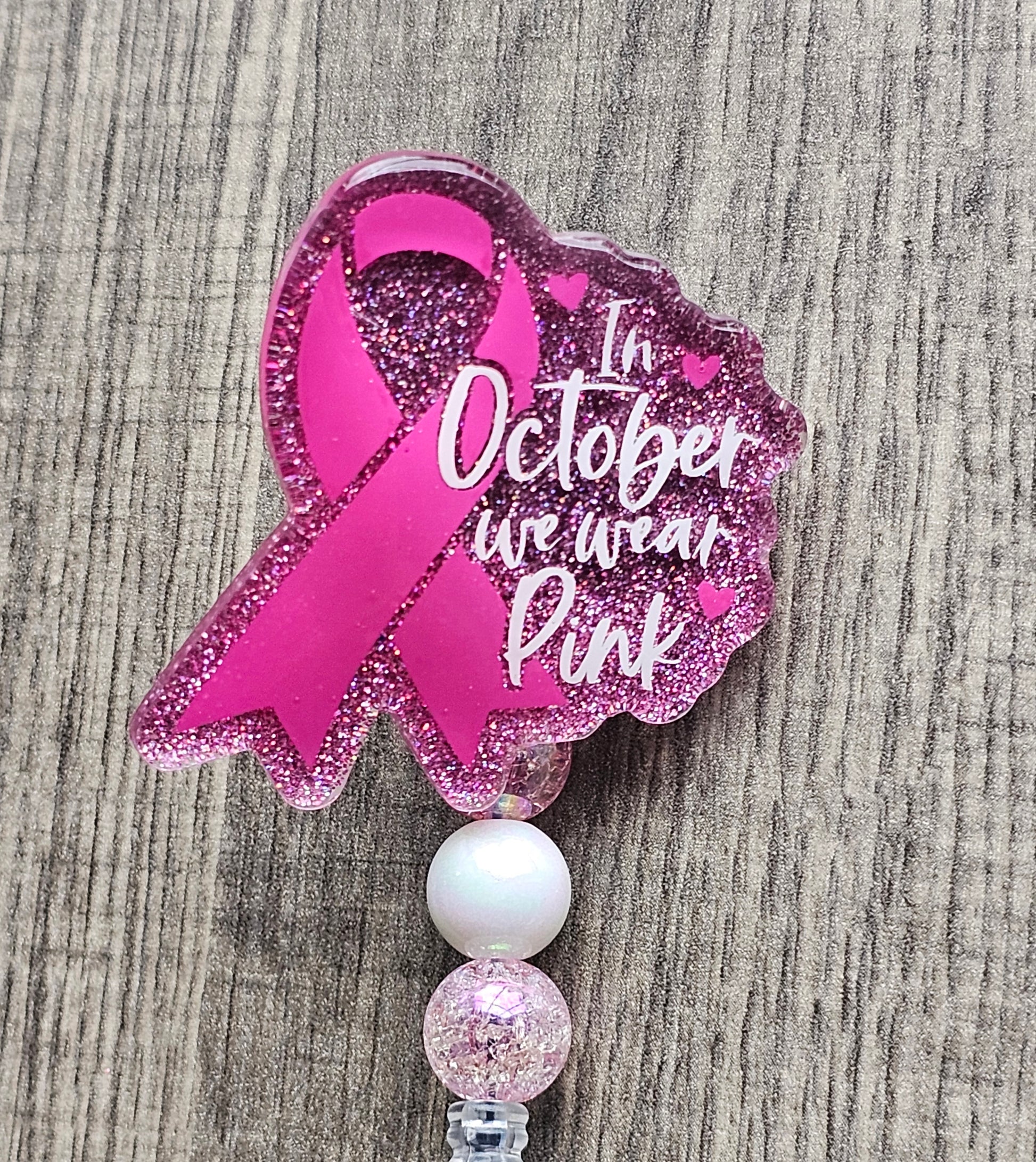 a pink badge reel stating in October we wear pink with the breast cancer awareness symbol