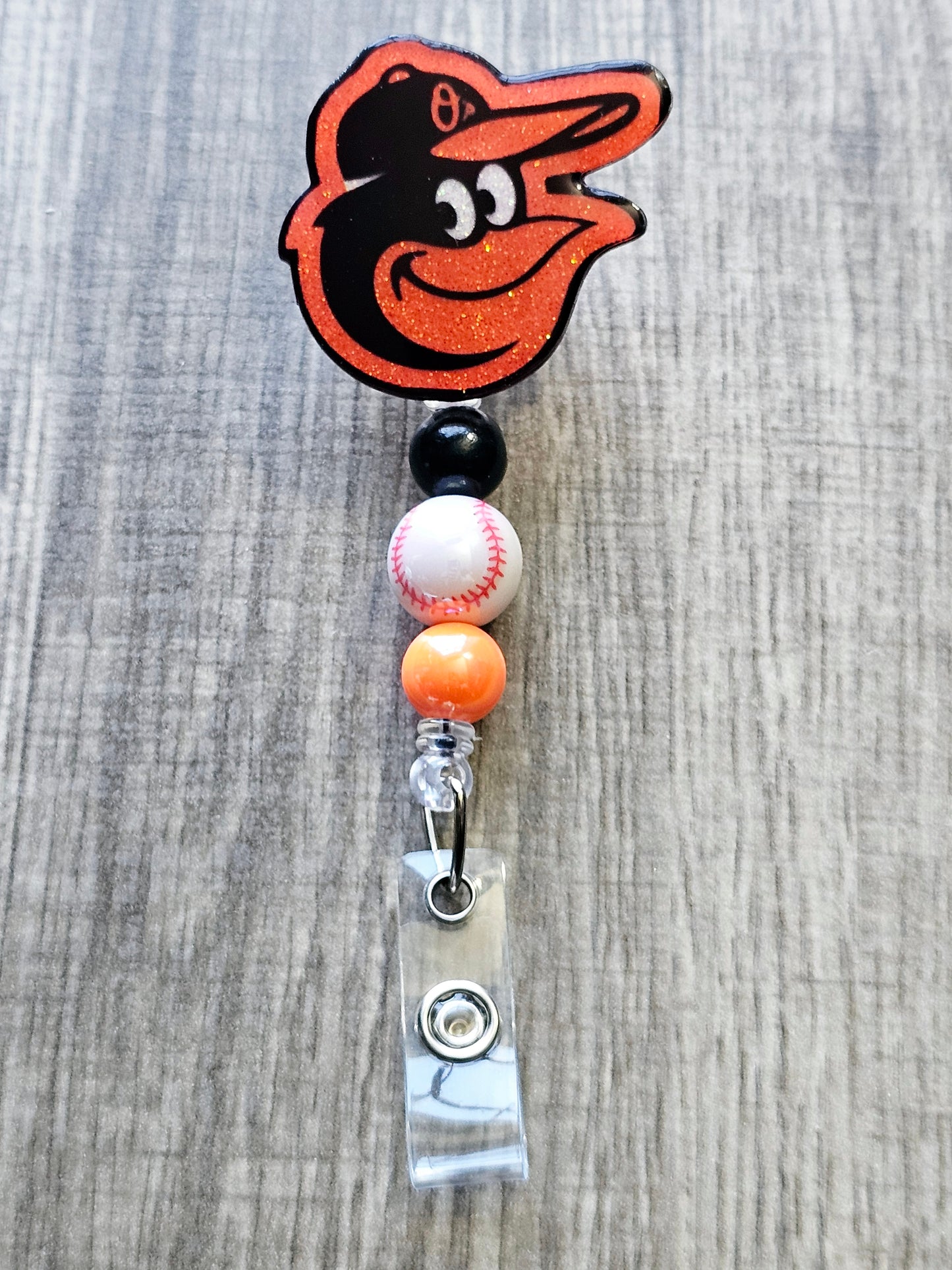 Handcrafted Orioles-inspired bird mascot badge reel with baseball beads glitter finish.