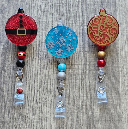Badge Reels one showcasing Santa's iconic outfit, another displaying delicate snowflakes falling against a turquoise background, and a third featuring a red ornament adorned with a beautiful golden pattern.