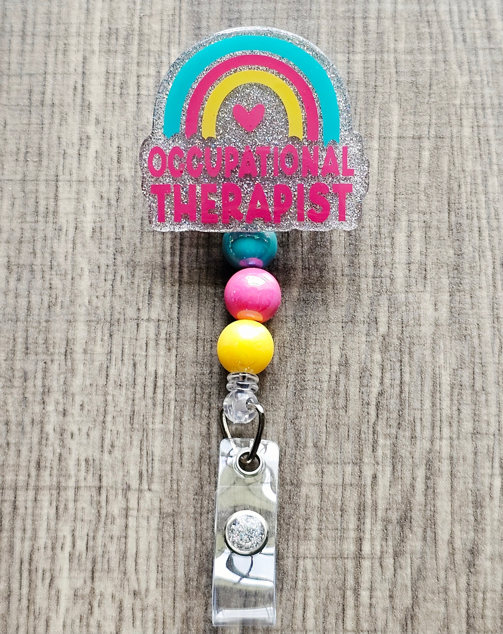 Occupational Therapist badge reel with silver glitter, rainbow, heart, and floral design.