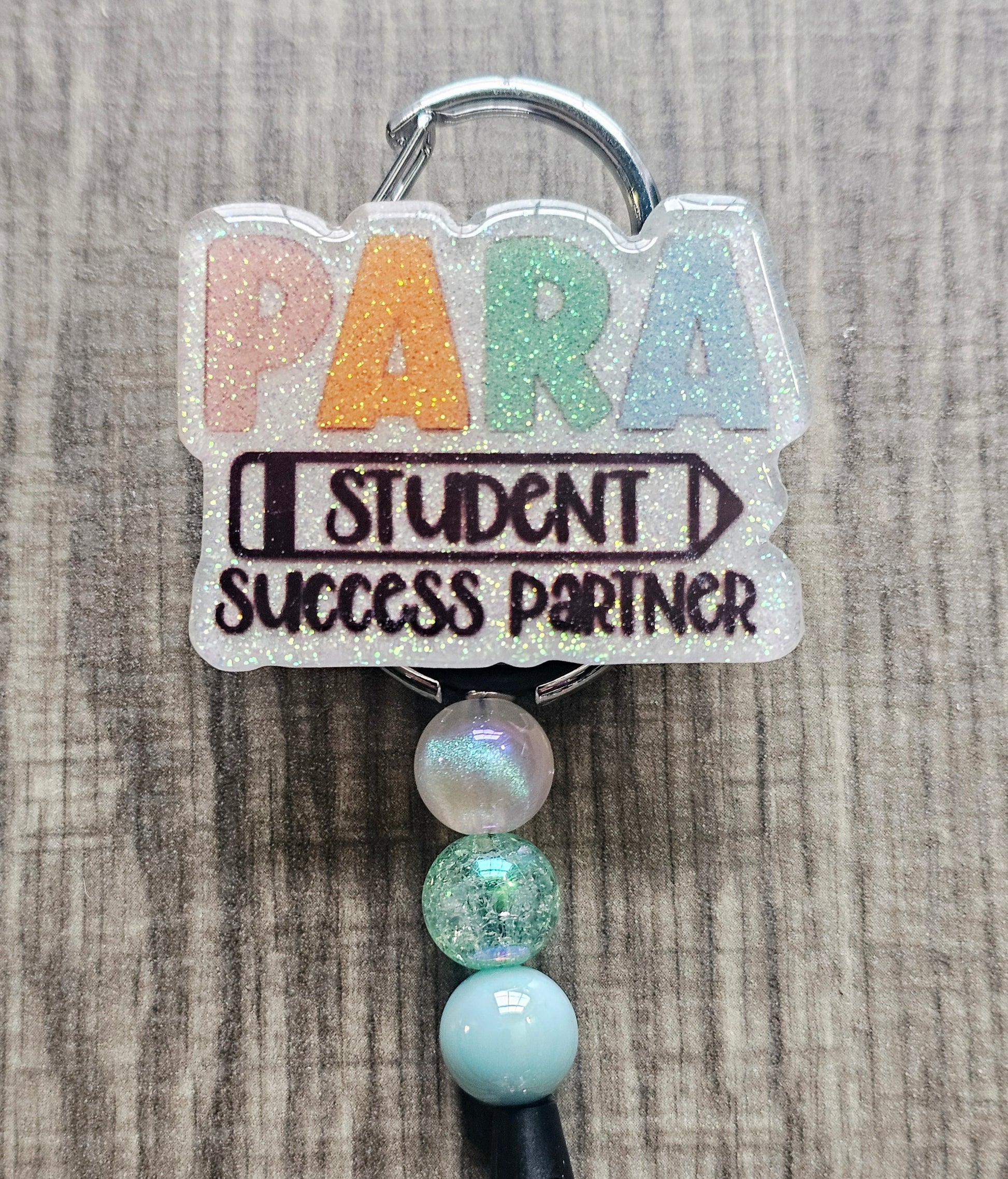 White glitter acrylic badge reel with "PARA," "Student" within a pencil, and "Success Partner" below, with well-coordinating decorative beads.