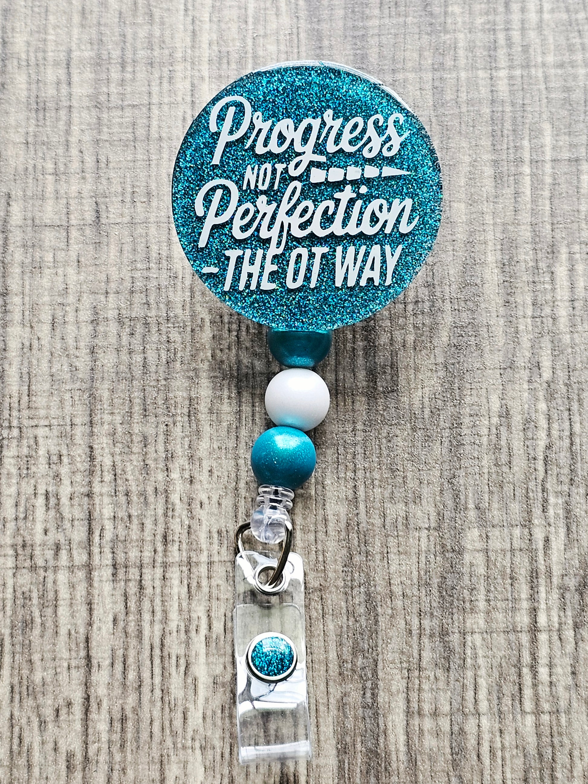 Turquoise 'Progress Not Perfection The OT Way' badge reel for Occupational Therapists.