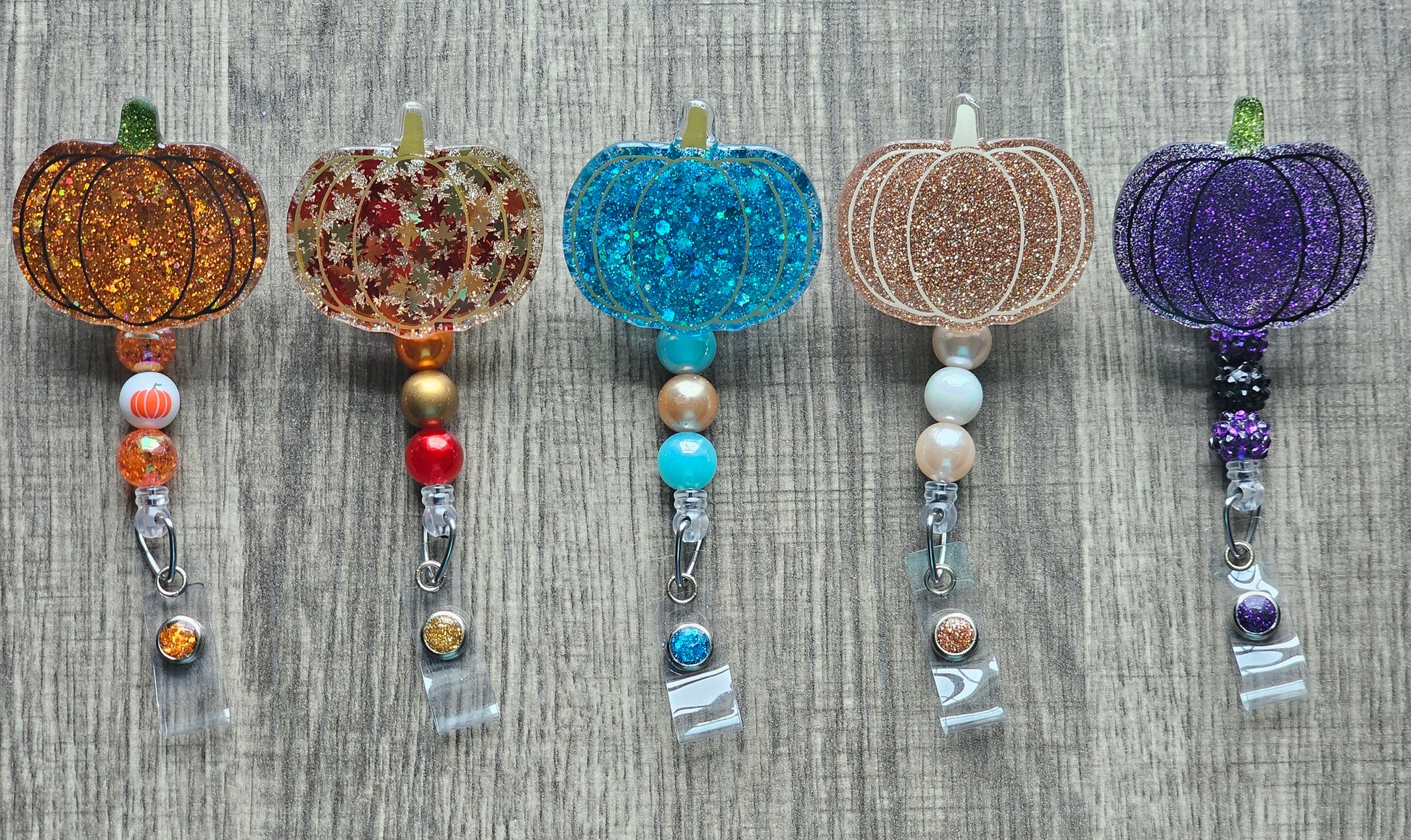 badge reels featuring pumpkin shaped badge reels ranging with the color turquoise, purple, rose gold, leaves design, as well as a traditional orange color