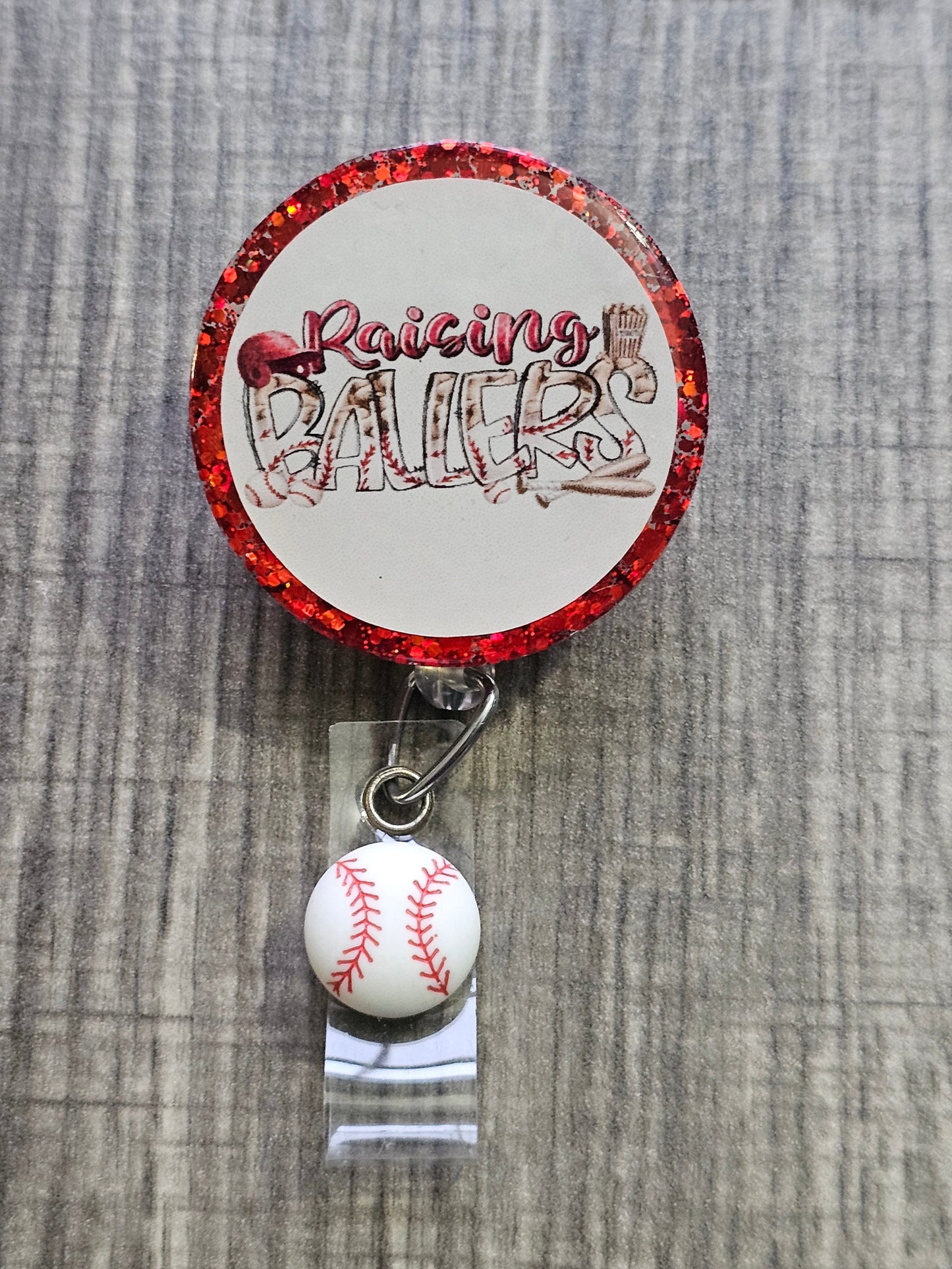 A Badge Reel with the statement Raising Ballers with a Baseball clip .