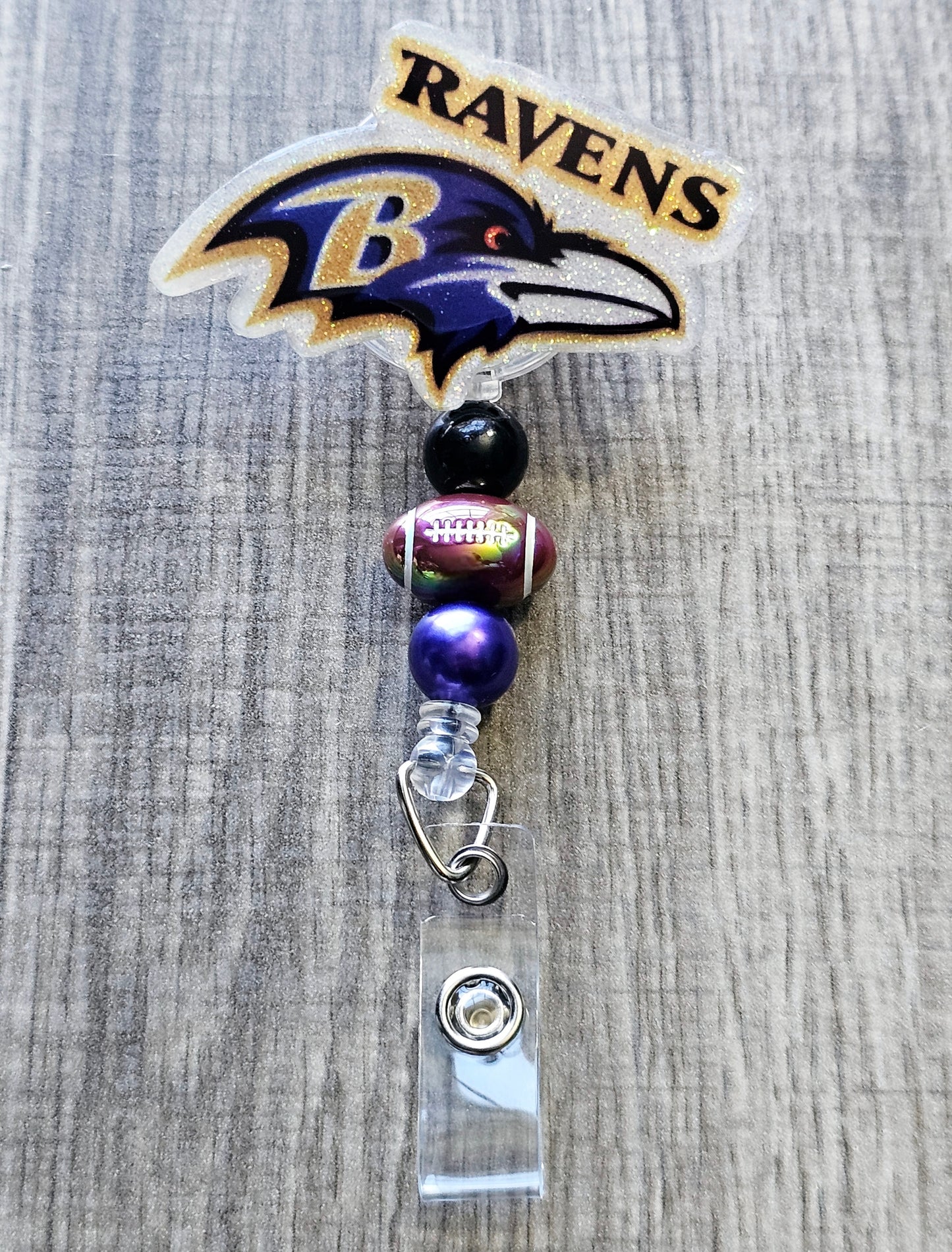 Ravens-inspired bird mascot badge reel with football beads, crafted in glitter acrylic.