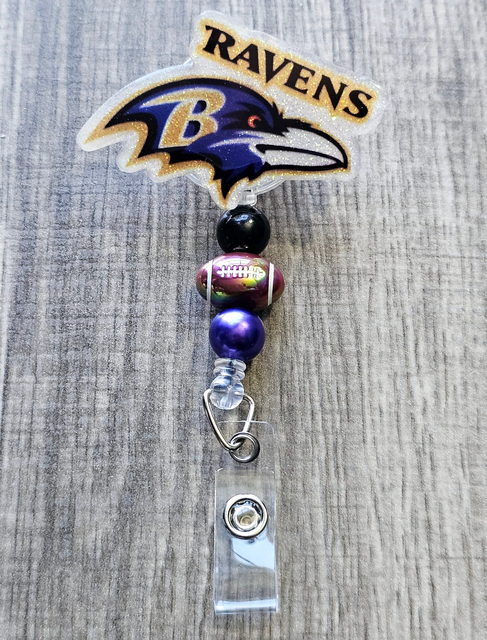 Ravens-inspired bird mascot badge reel with football beads, crafted in glitter acrylic.