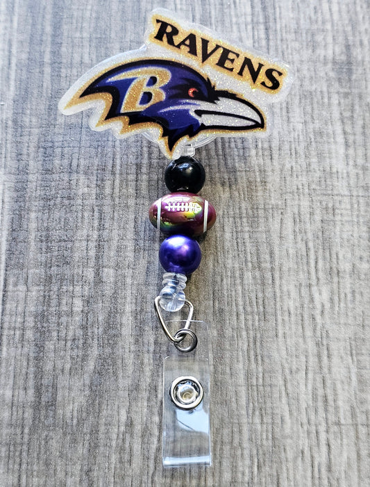 Ravens-inspired bird mascot badge reel with football beads, crafted in glitter acrylic.