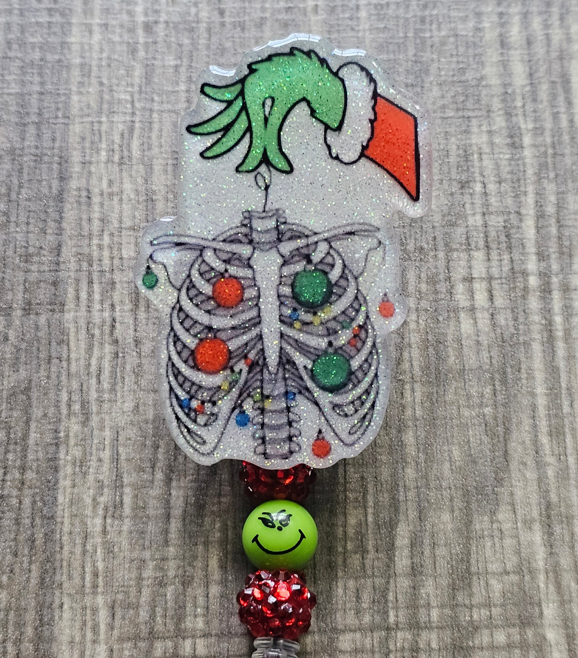 A badge reel displaying the hand of the grinch with a Christmas sweater holding a chest x-ray adorned with christmas lights and ornaments