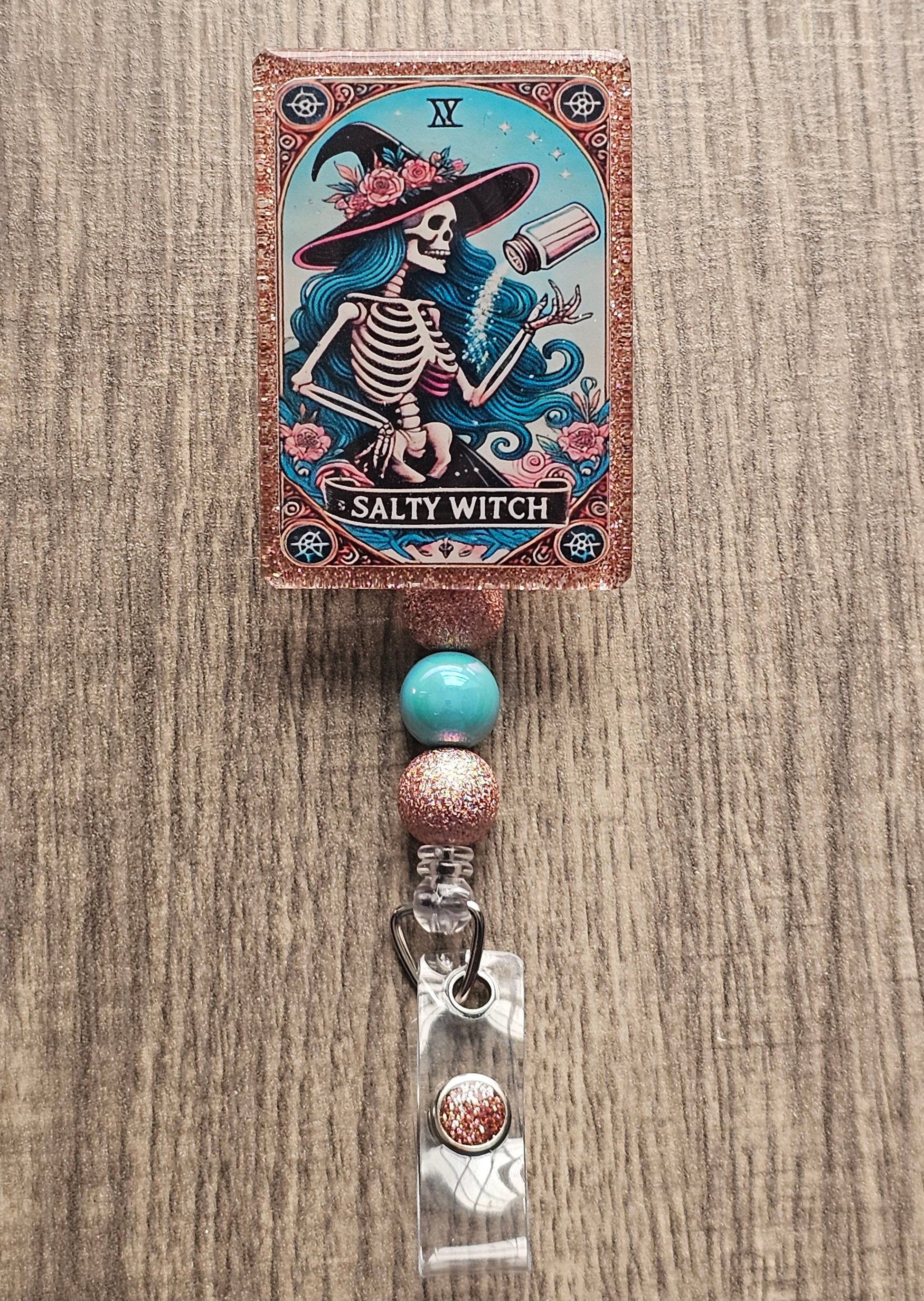 Badge reel shaped as a tarot card featuring a female skeleton witch making salt levitate with the title salty witch