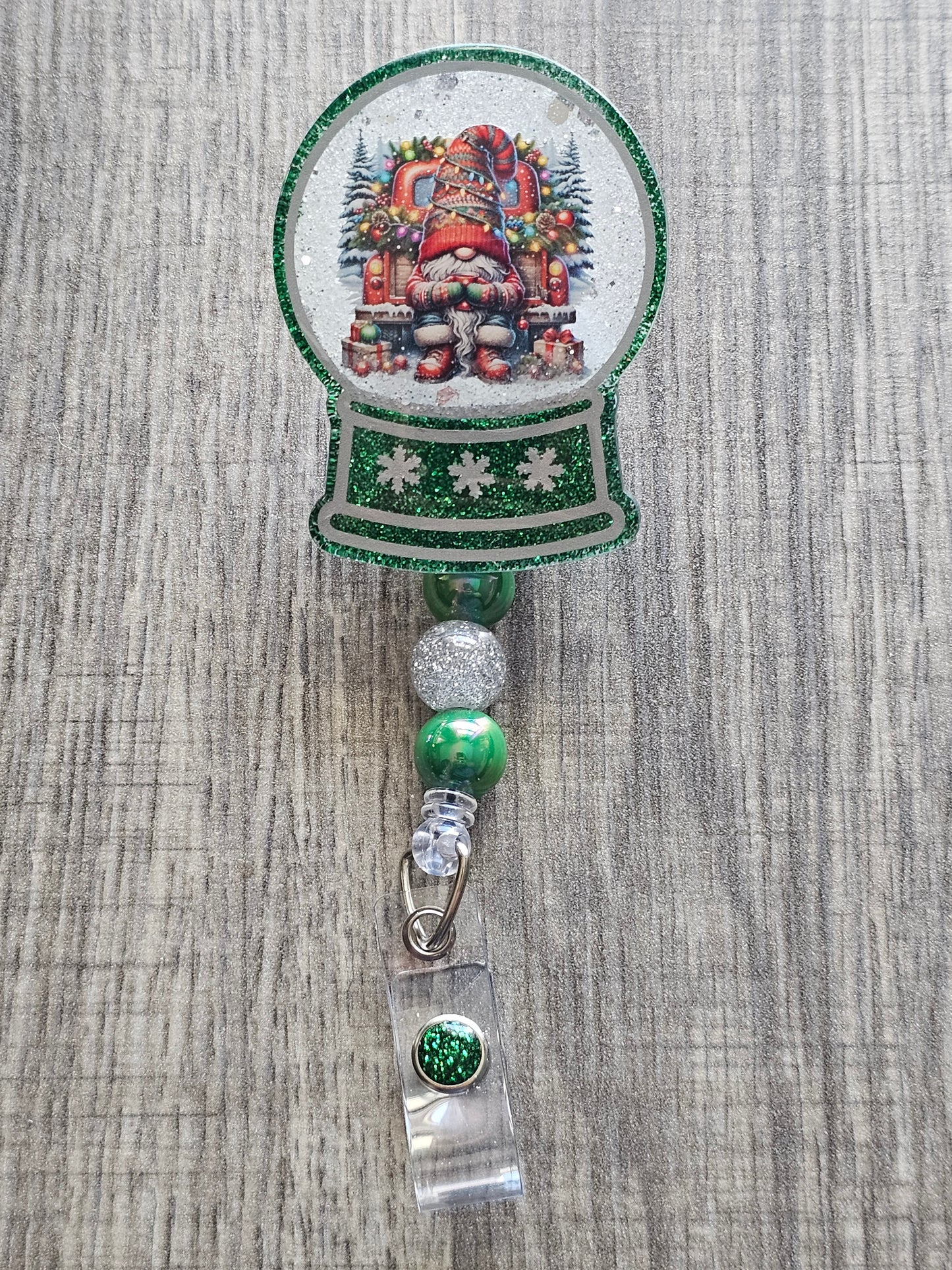 A badge reel with a snow globe design featuring a festive gnome dressed in a Christmas Sweater, drinking chocolate on the back of a truck with festive decorations surrounded by Christmas Presents.