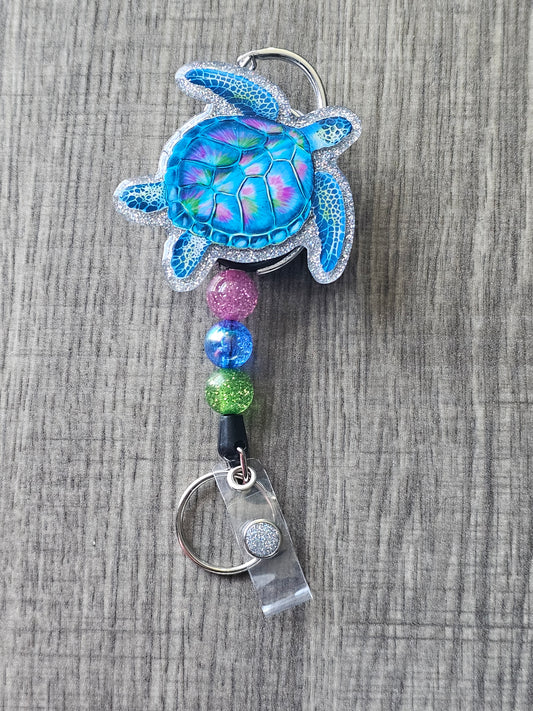 A Badge Reel displaying a florescent sea turtle on a carabiner lanyard clip.
