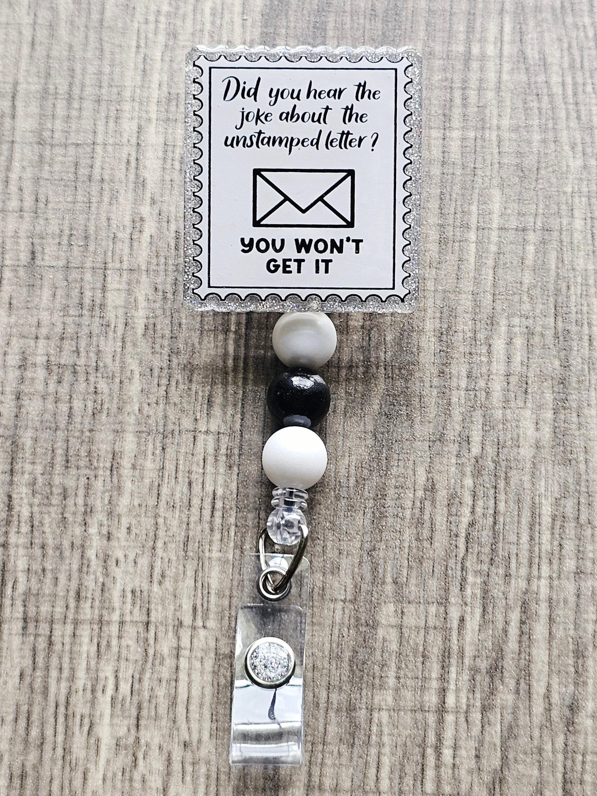 Stamp-shaped badge reel with a mail joke that says “Did you hear the joke about the unstamped letter? You won’t get it.