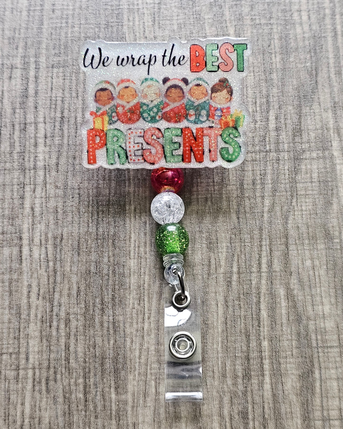 A badge reel stating we wrap the best presents with the design incorporating some adorable children wrapped in cozy festive blankets