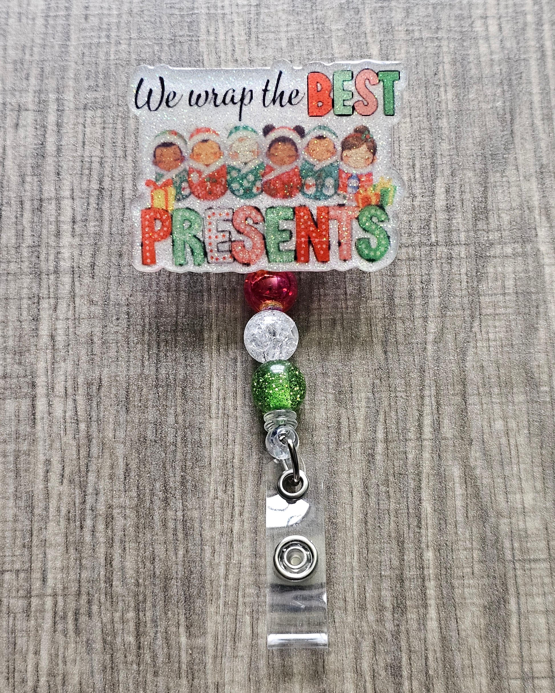 A badge reel stating we wrap the best presents with the design incorporating some adorable children wrapped in cozy festive blankets