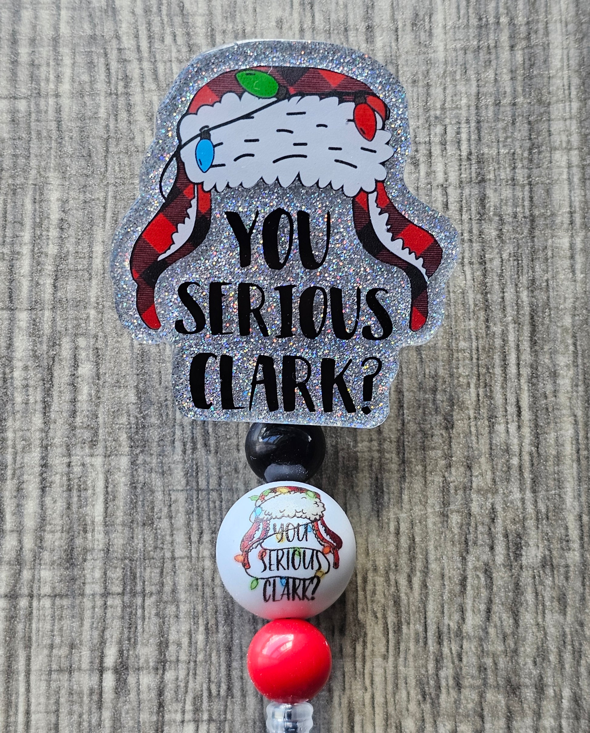 A Badge Reel featuring a Christmas themed winter hat wrapped with Christmas lights and underneath it with the words You Serious Clark?