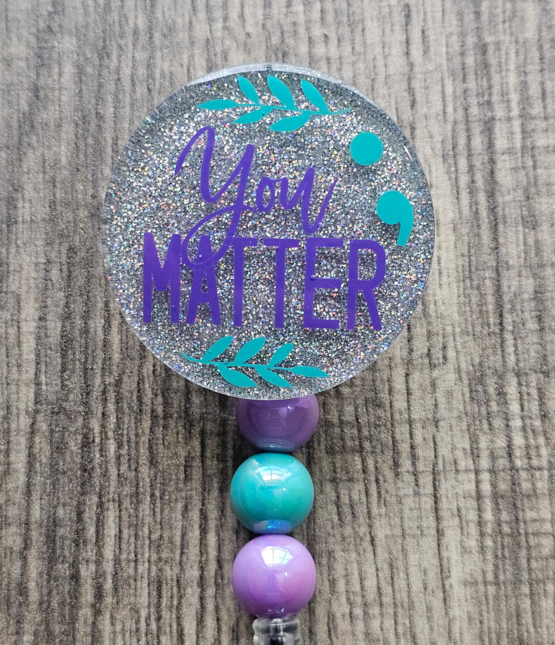 a silver badge reel stating you matter in purple along with a semi colon