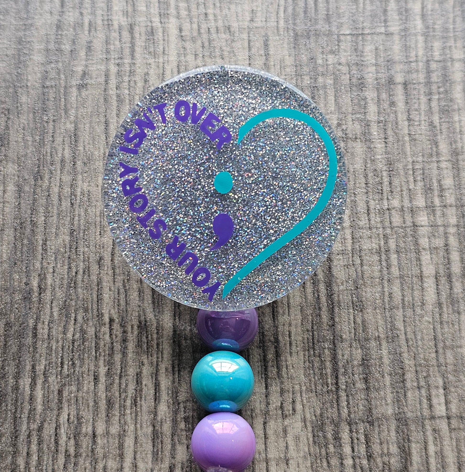 Silver badge reel stating Your story isn't over shaped in the form of a heart along with a semicolon in the middle