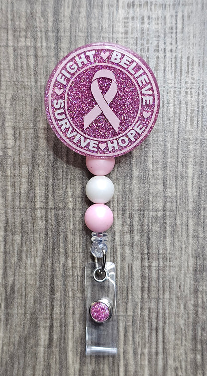 Pink glitter badge reel with breast cancer awareness ribbon on a textured surface