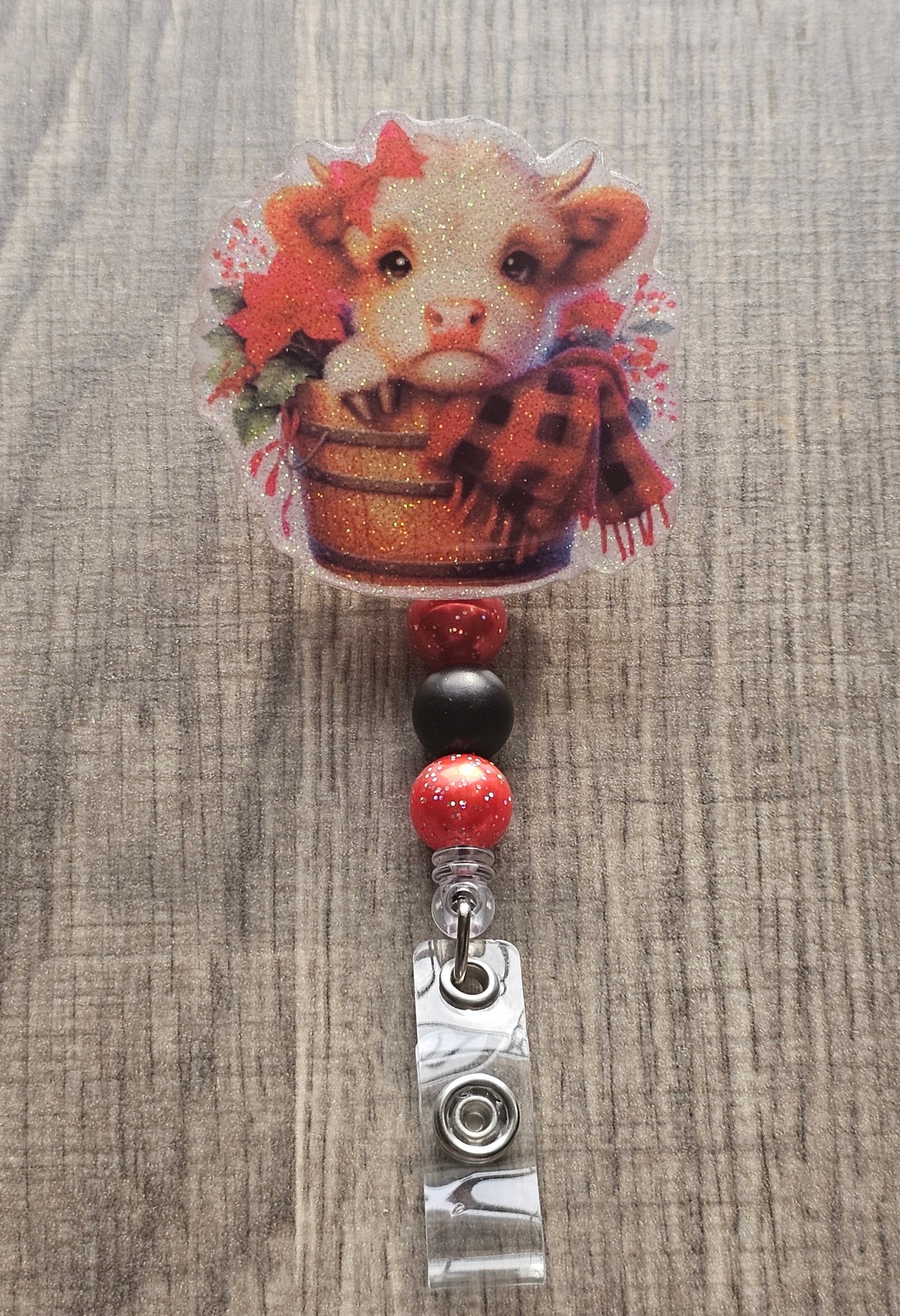 This badge reel showcases an adorable highland cow nestled in a cozy bucket, draped with a soft blanket and surrounded by delicate flowers.