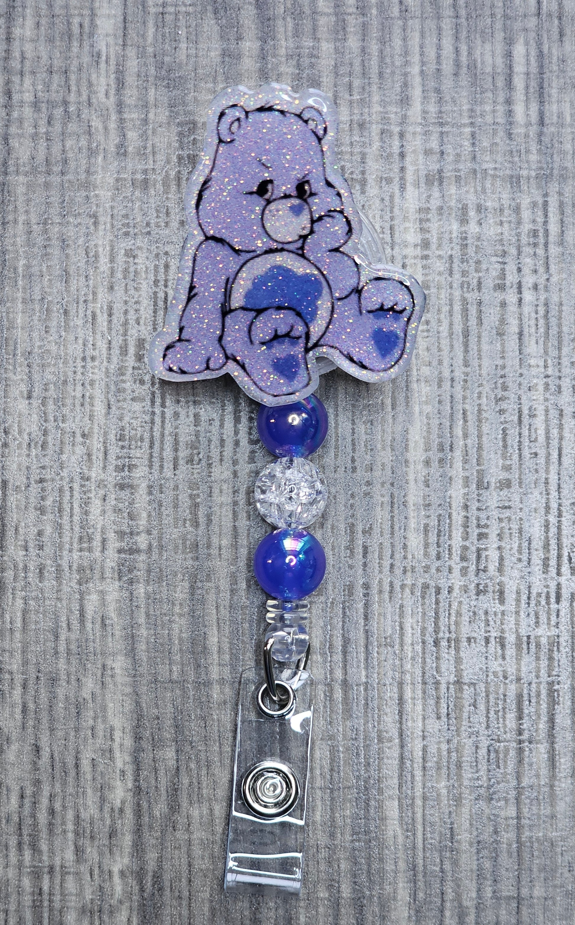 Grumpy Care Bear-shaped badge holder with blue and silver beads on a textured gray background