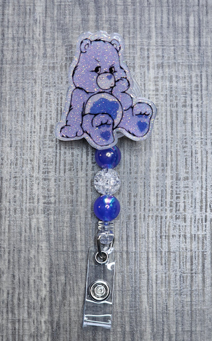 Grumpy Care Bear-shaped badge holder with blue and silver beads on a textured gray background