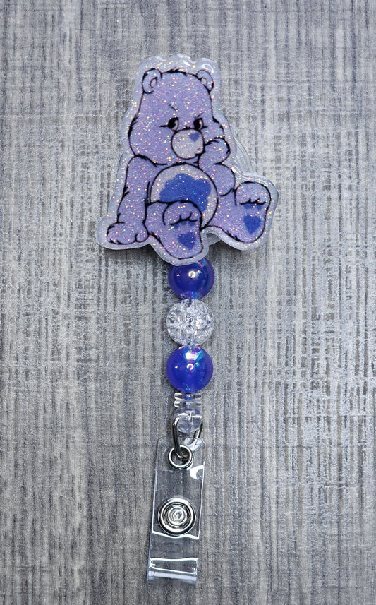 Grumpy Care Bear-shaped badge holder with blue and silver beads on a textured gray background