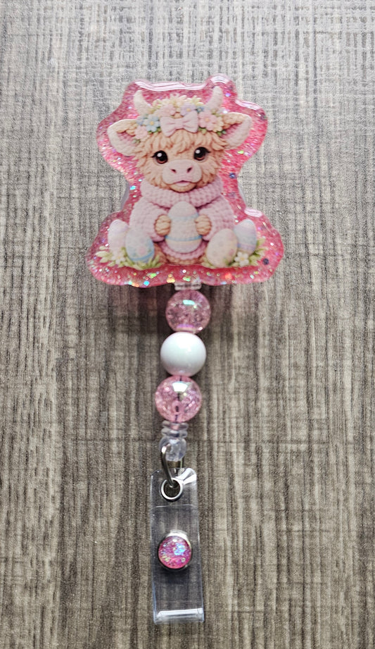Retractable badge reel showing a brown highland cow wearing a pink sweater, surrounded by colorful Easter eggs.