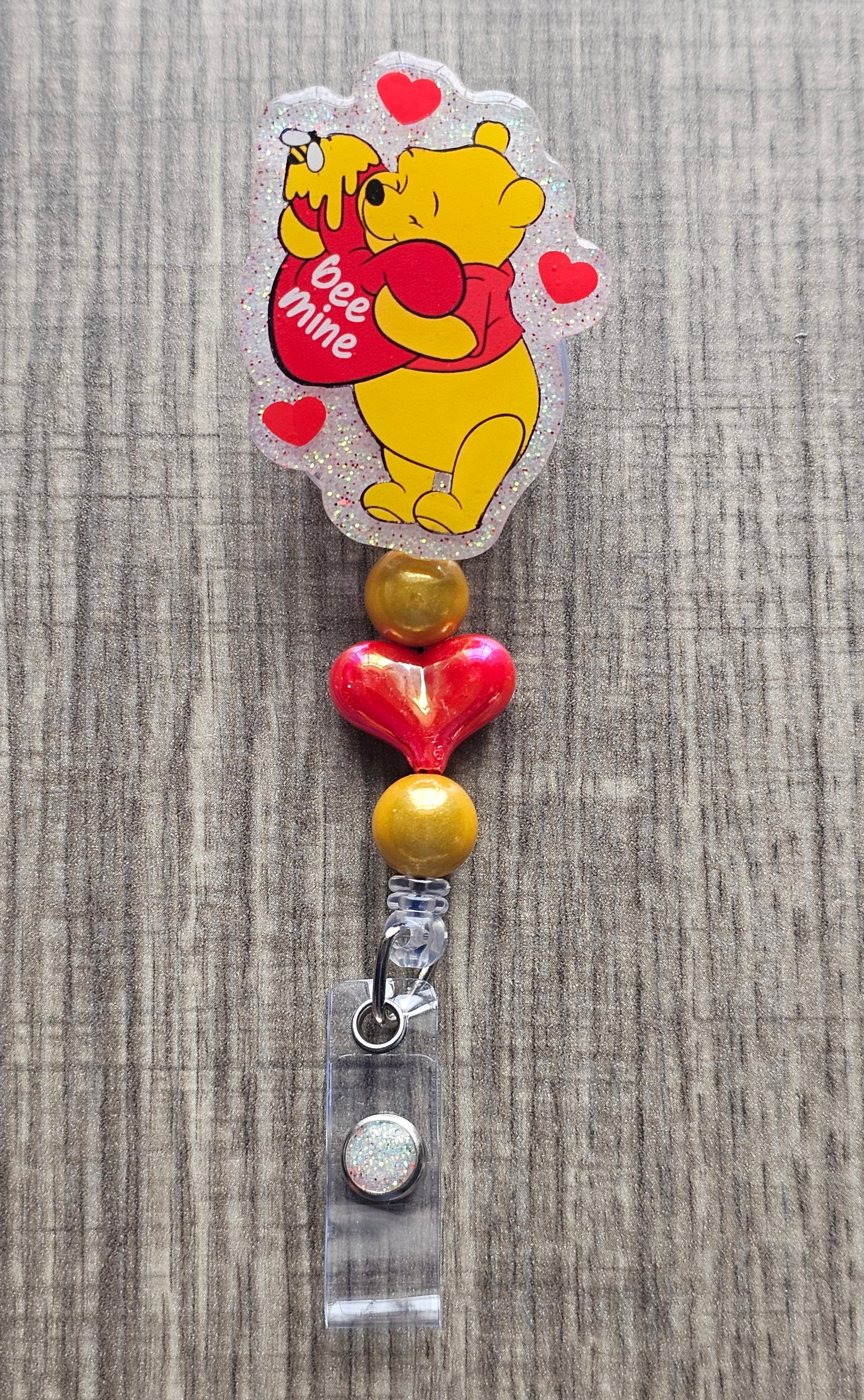 Retractable badge reel with Winnie the Pooh hugging a heart that says Bee Mine with honey drips.