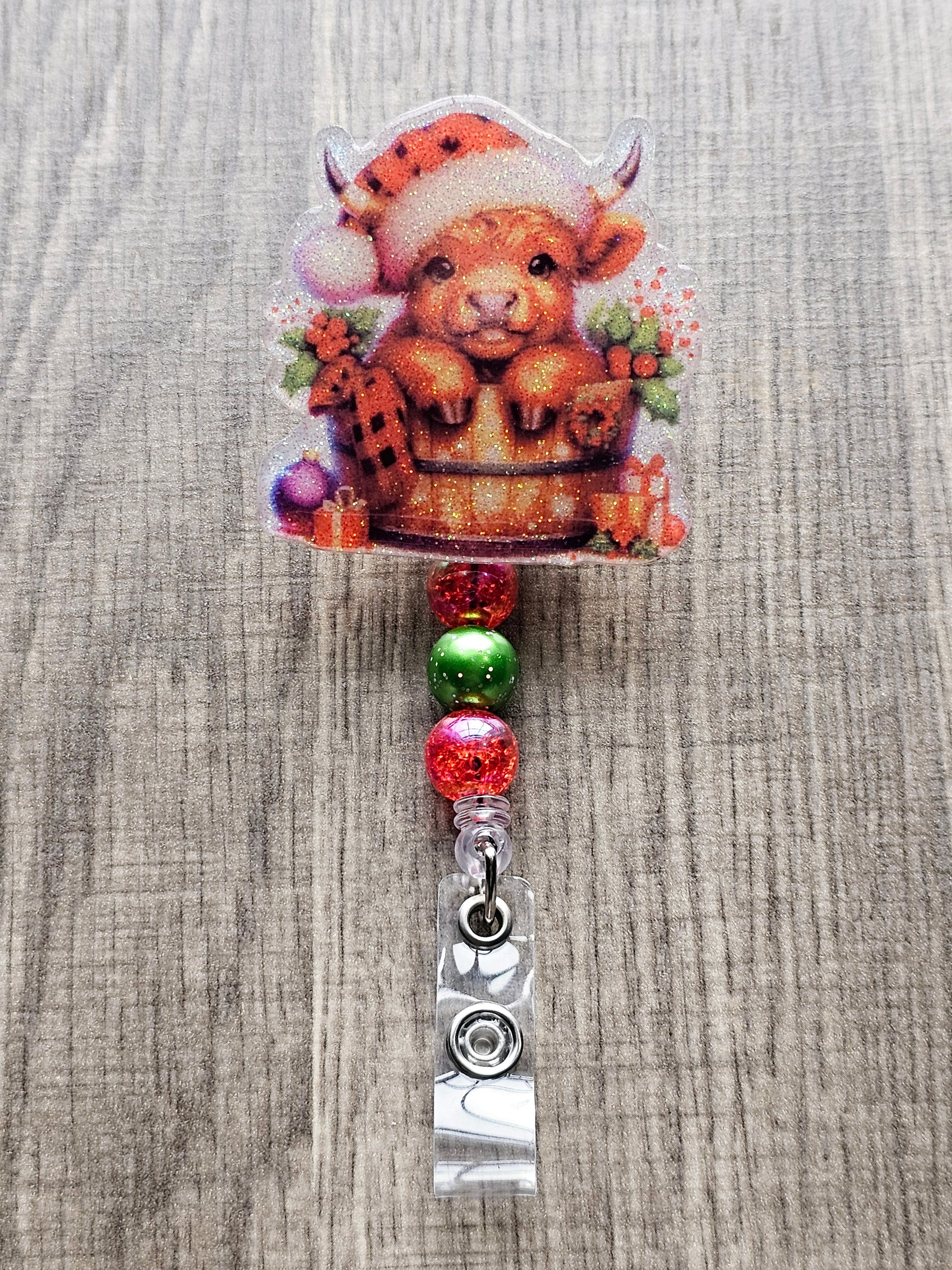 A badge reel that showcases an adorable highland cow nestled in a bucket, wrapped in a cozy blanket, adorned with vibrant flowers, Christmas ornaments, and charmingly wrapped gifts. Topped with a plaid Christmas hat.